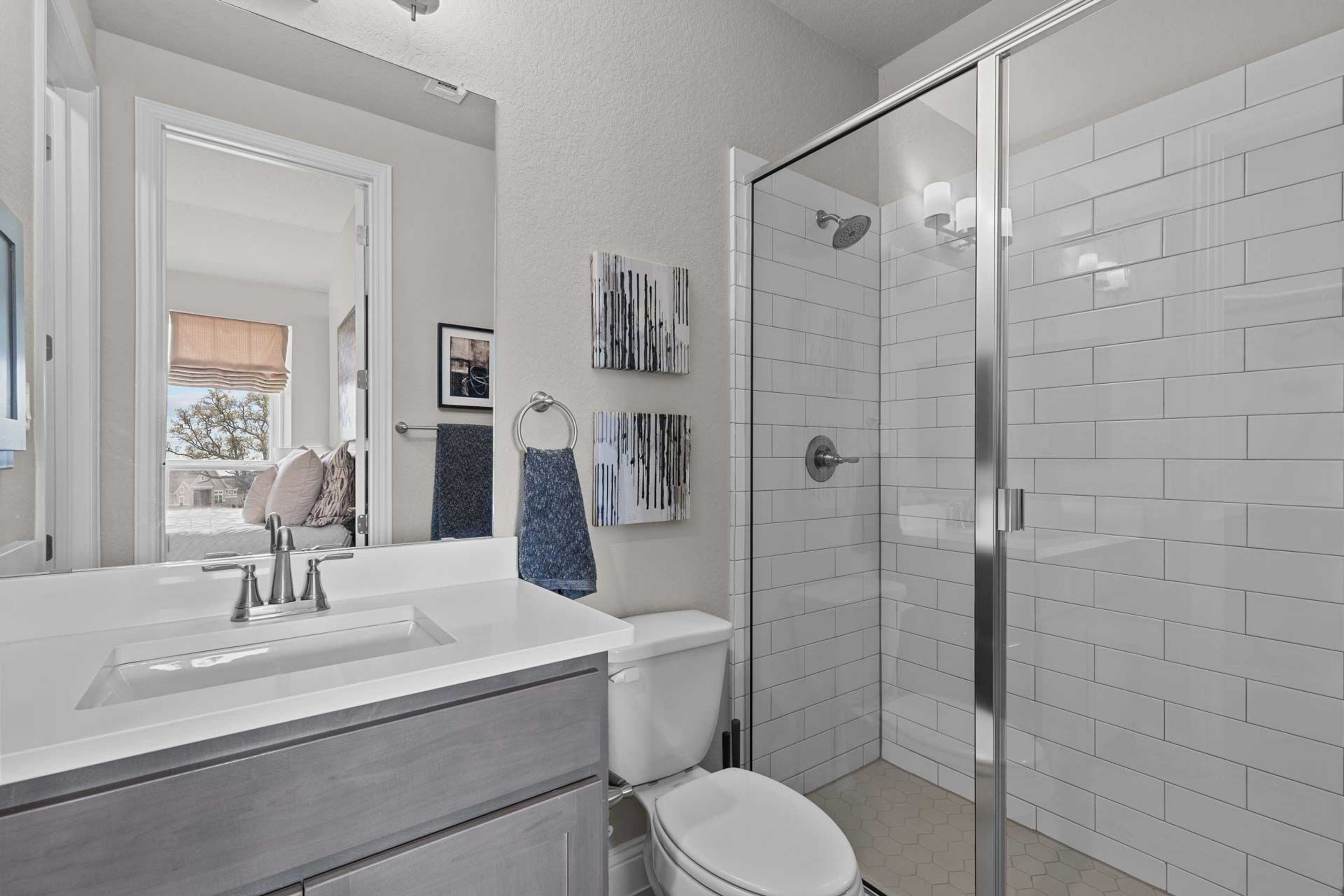 Modern bathroom in Ladera San Antonio with glass shower white subway tiles gray vanity blue towels and framed art by Davidson Homes