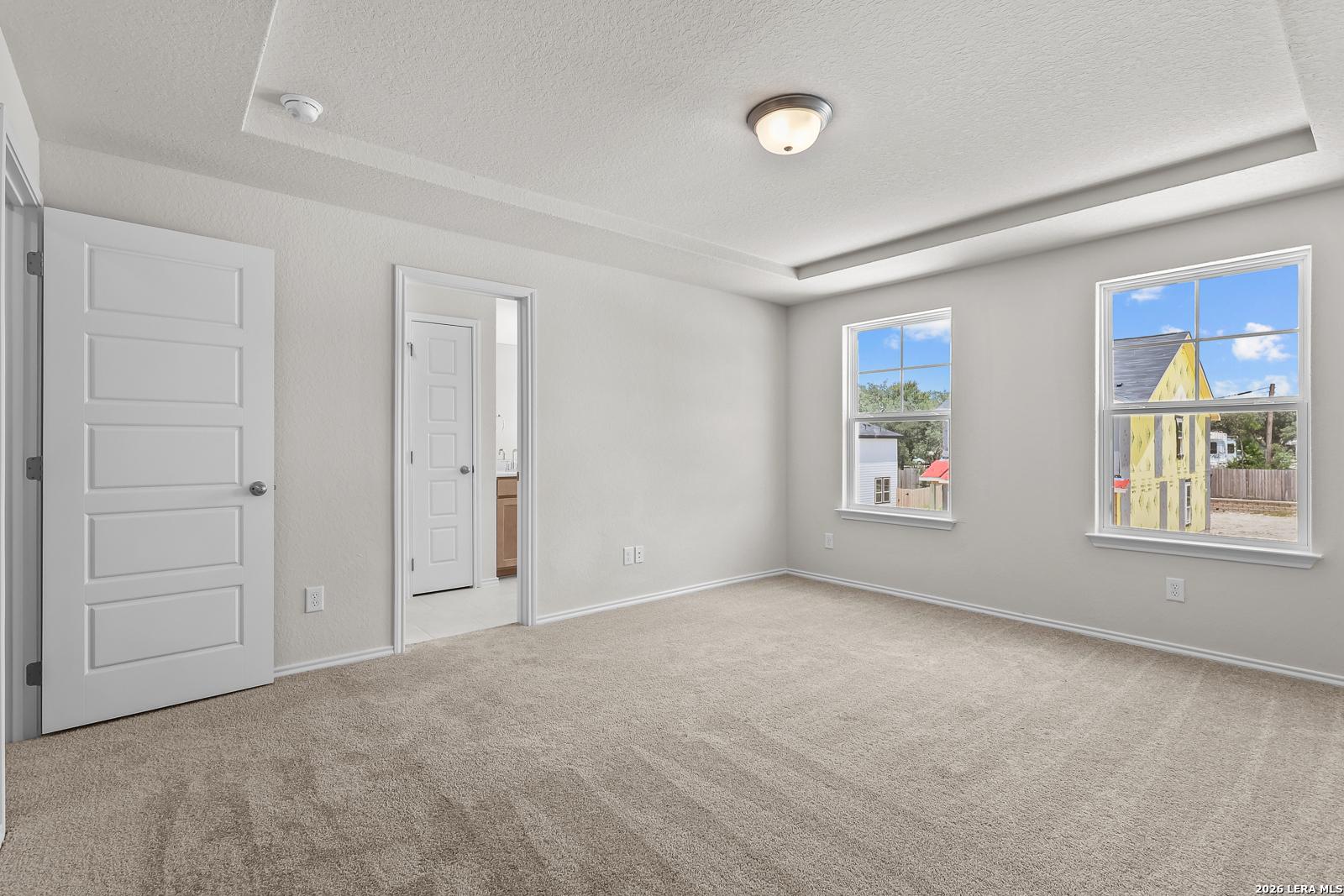 Bright primary bedroom with tray ceiling and en-suite bathroom in The Gillian B floor plan at Meadows at Oak Creek.