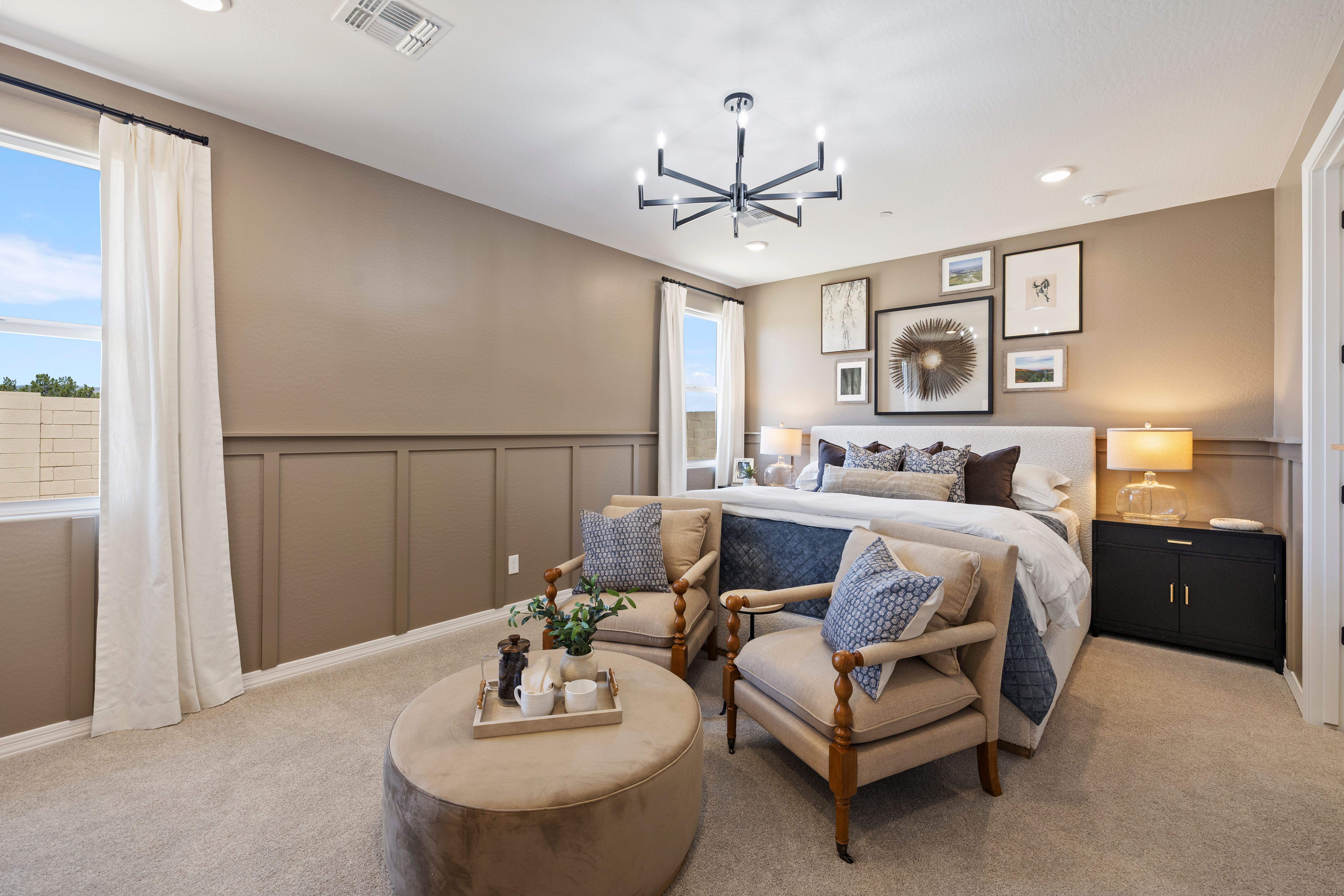 Cozy master bedroom at Vineyards at Cottonwood in Cottonwood AZ with beige wainscoting, king bed, blue accent chairs, ottoman, and chandelier