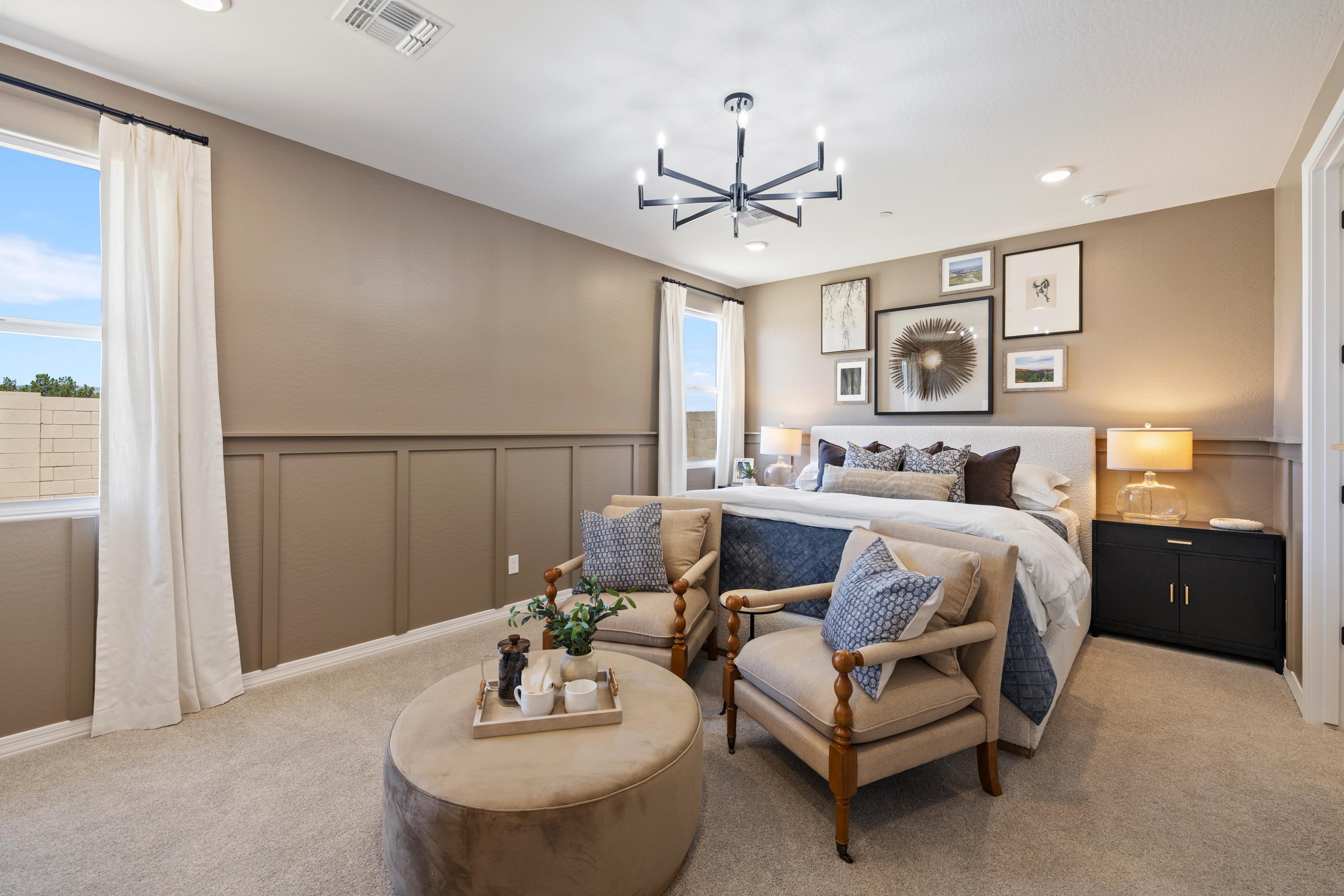 Cozy master bedroom at Vineyards at Cottonwood in Cottonwood AZ with beige wainscoting, king bed, blue accent chairs, ottoman, and chandelier