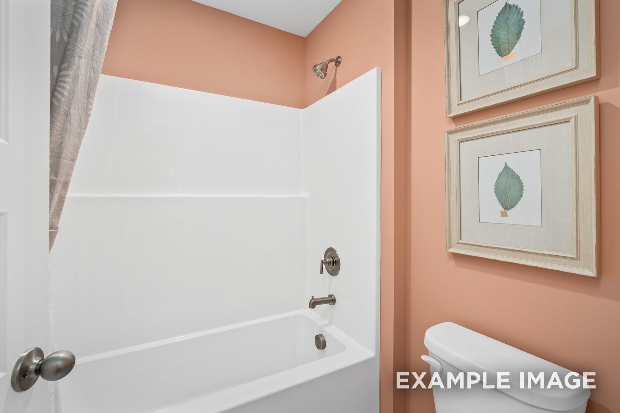 Cozy bathroom with white tub-shower combo, peach walls, leaf art in Davidson Homes The Ash A, Gallatin, Tennessee