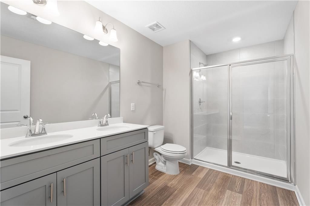 Modern master bathroom with double gray vanity, frameless glass shower, and wood flooring in Davidson Homes The Washington, Phenix City