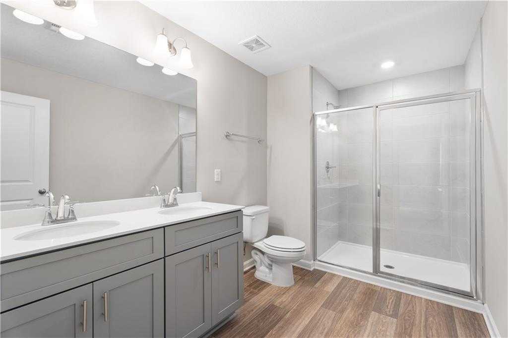 Modern master bathroom with double gray vanity, frameless glass shower, and wood flooring in Davidson Homes The Washington, Phenix City