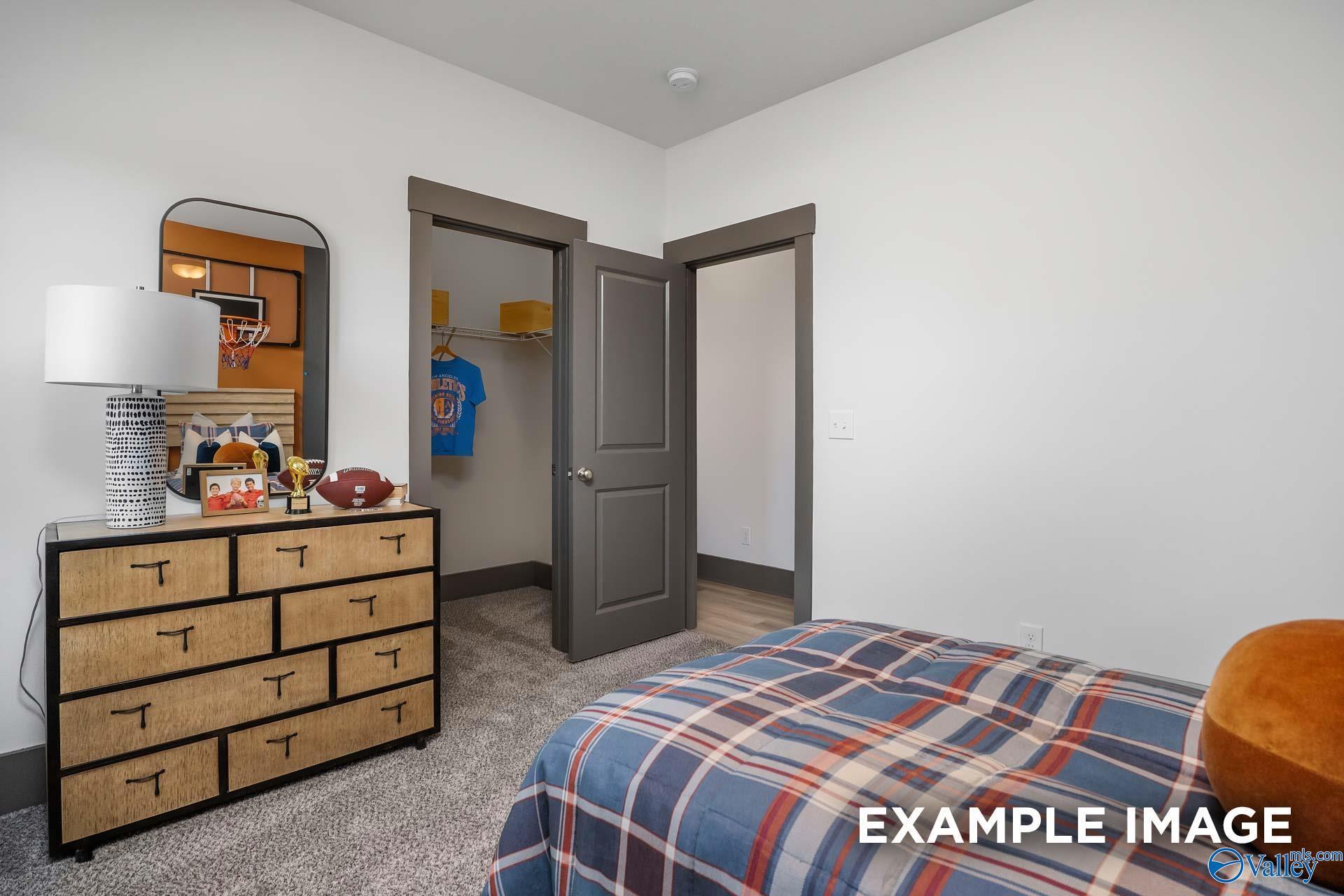 Cozy sports-themed child's bedroom with plaid bedding, wooden dresser, lamp with memorabilia, and blue jersey in Davidson Homes The Rockford B, Madison, Alabama
