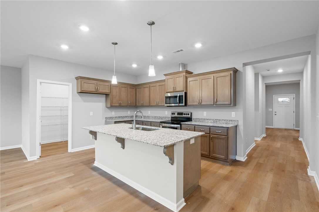 Modern white shaker kitchen with quartz island sink, stainless appliances, and hardwood floors in The Luna B, Opelika, AL