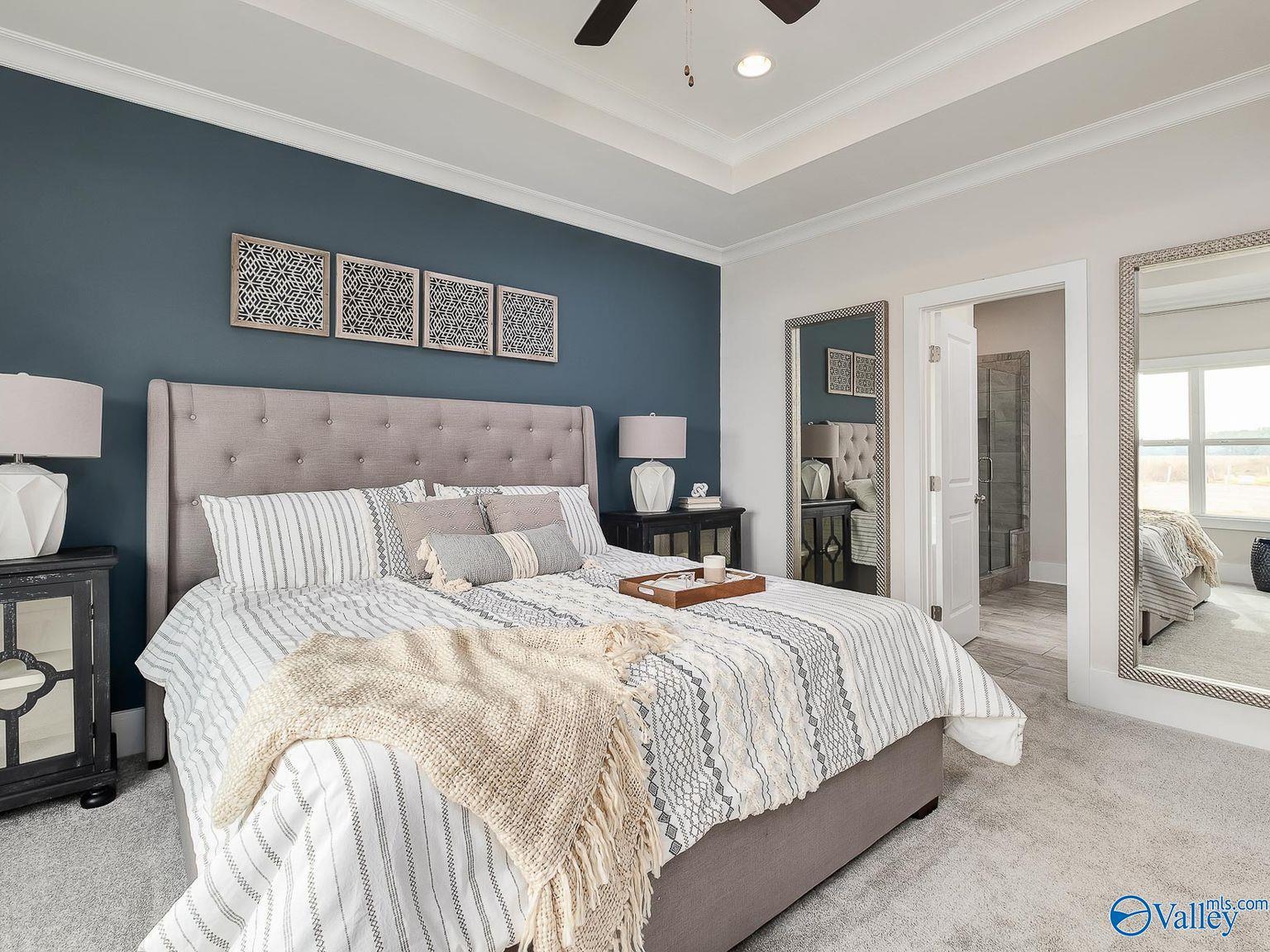 Luxurious master bedroom with navy accent wall, tufted king bed, striped bedding, tray ceiling in Davidson Homes The Everett, Toney, Alabama