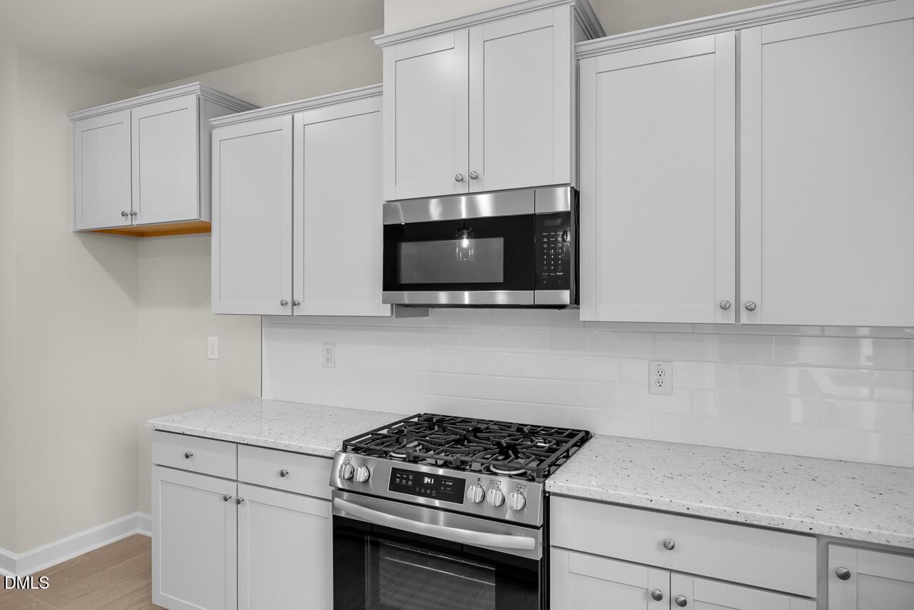 Modern kitchen with white shaker cabinets, stainless steel gas range, microwave, quartz countertops in Davidson Homes The Avery, Knightdale, NC