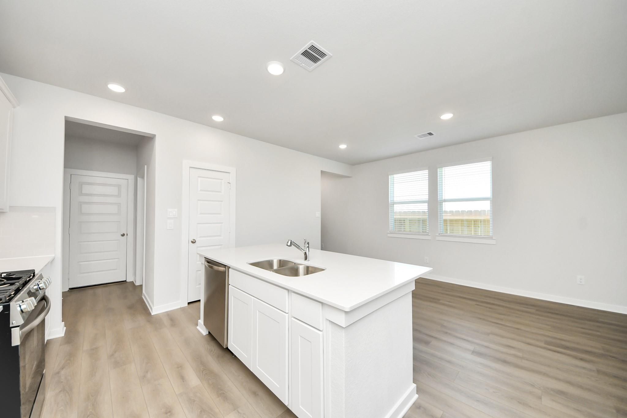 Modern kitchen with white island, stainless appliances, and wood-look flooring in The Costa A home at Emberly, Beasley, TX.