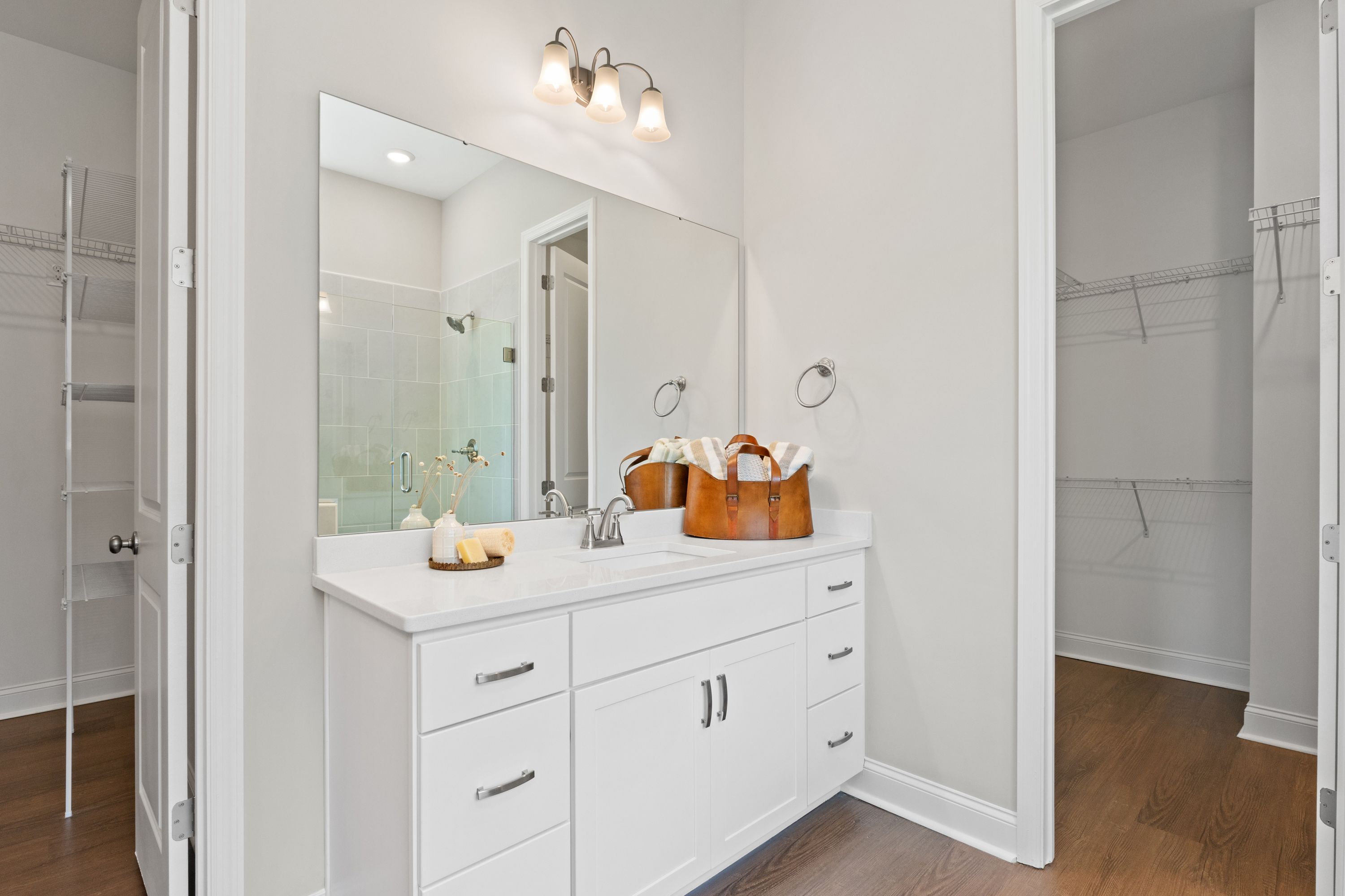 Spacious master bathroom in The Haven D with double white vanity, large mirror, sconce lighting, and walk-in closet