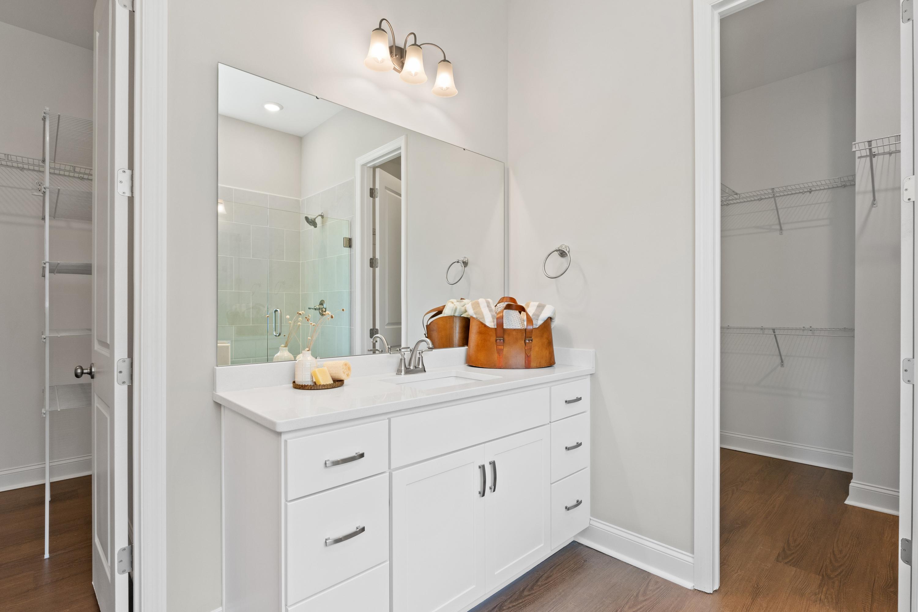 Spacious master bathroom in The Haven D with double white vanity, large mirror, sconce lighting, and walk-in closet