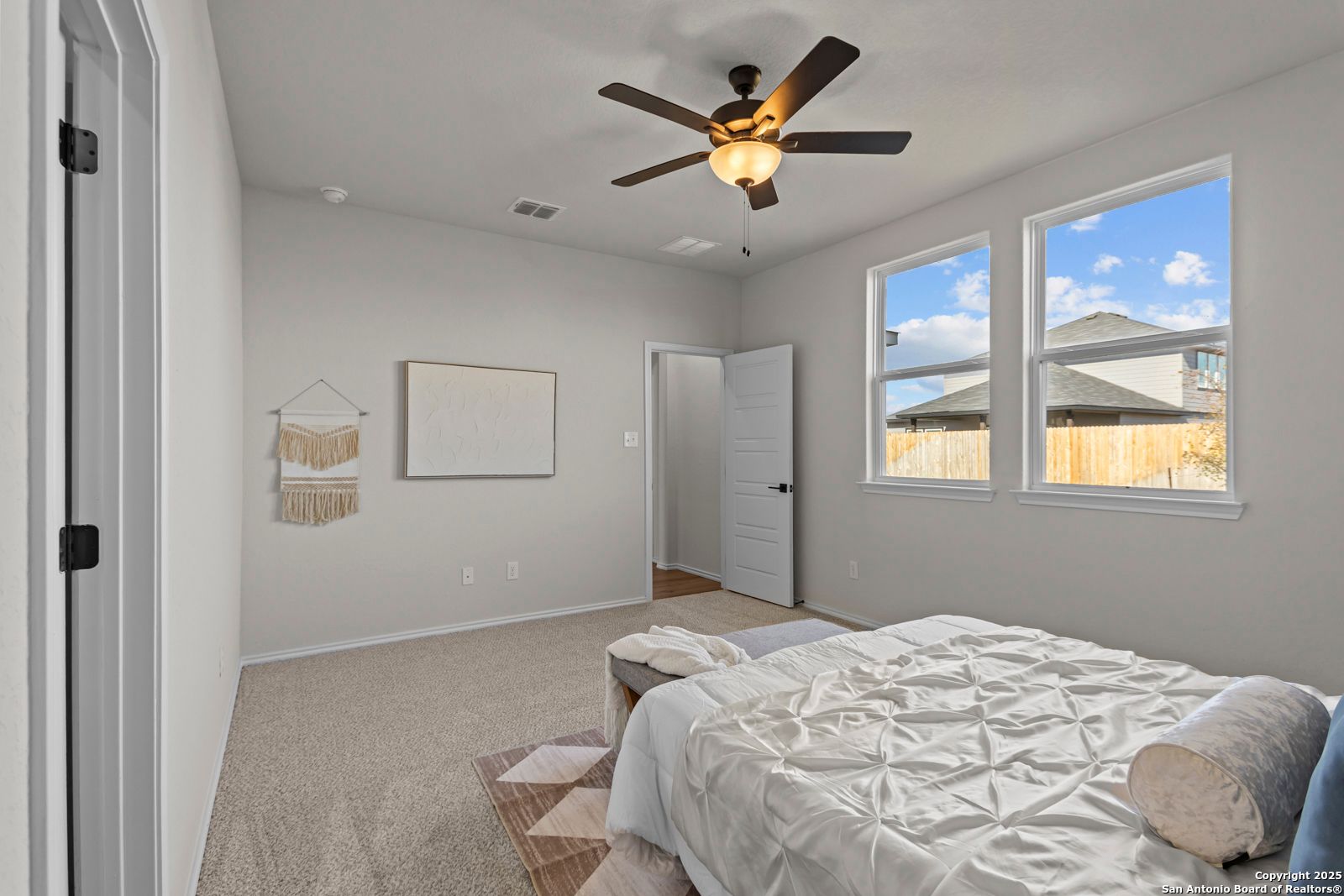 Bright master bedroom with plush white bedding, ceiling fan, and large windows overlooking backyard in Davidson Homes The Douglas C, Seguin, Texas