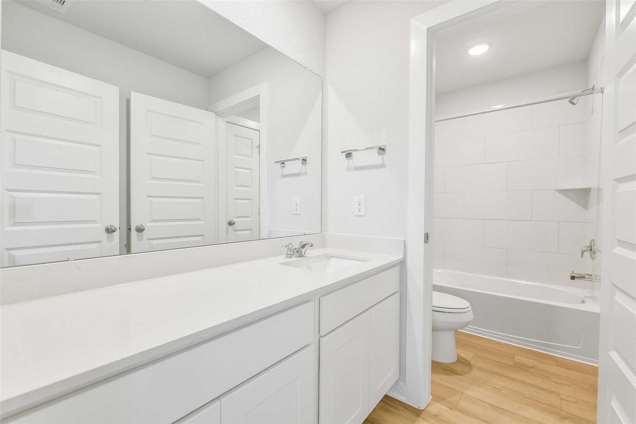 Bright white double vanity bathroom with bathtub, shower, and light wood floors in Davidson Homes The San Marcos E, Cleveland, Texas