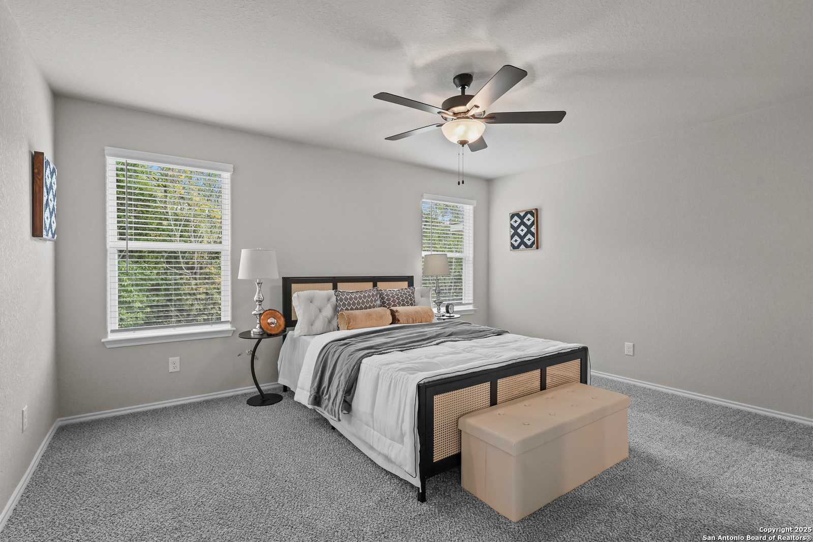 Cozy bedroom with black-framed king bed, ceiling fan, and window views in Davidson Homes The Charlotte B, San Antonio, Texas