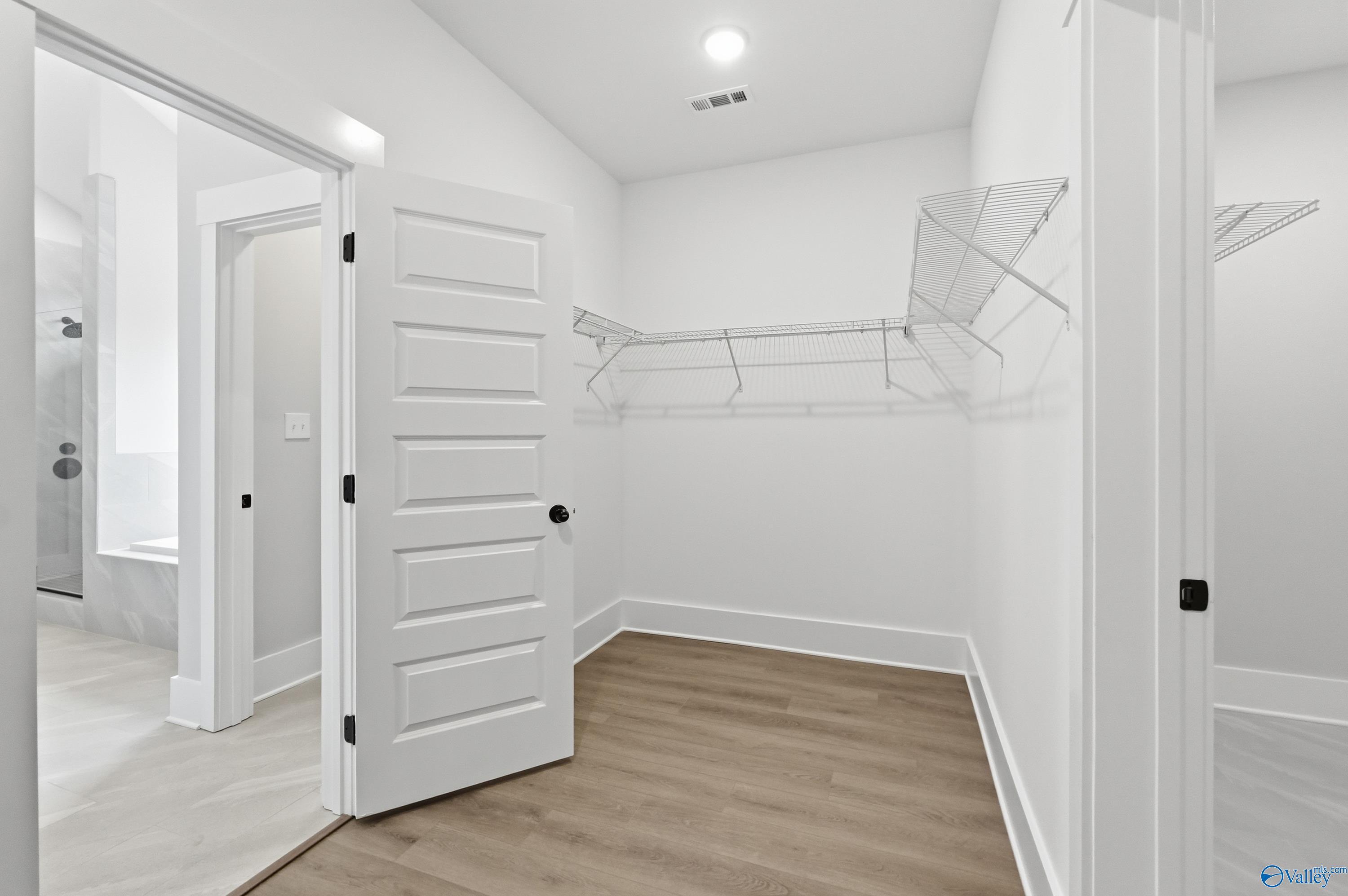 Spacious walk-in closet with white shelving, open doors, and adjacent master shower in Davidson Homes The Finleigh, Meridianville, Alabama