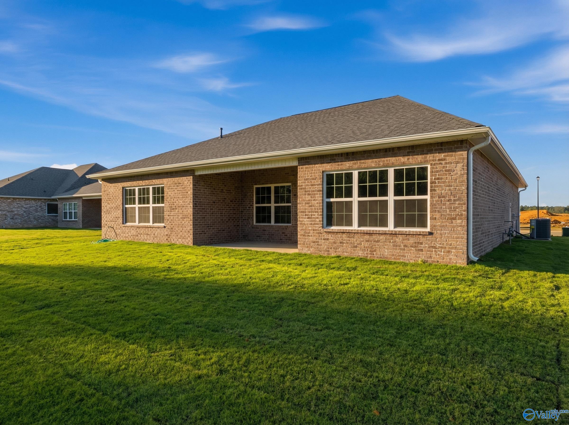 Rear view of brick single-story Montgomery B home with covered patio, large windows, and lush green lawn in Cain Park, Hartselle, Alabama