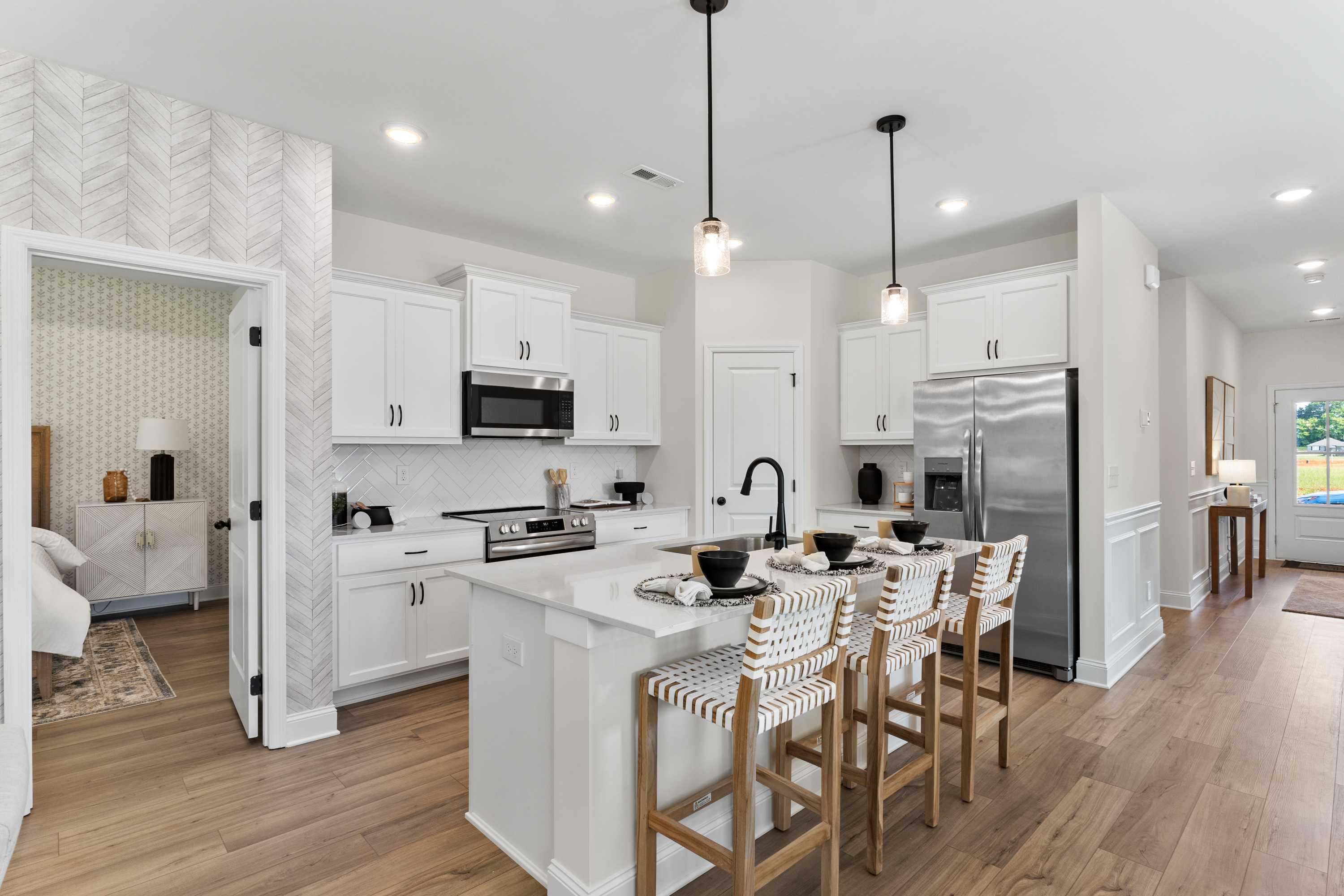 Open-concept white kitchen with island, bar stools, and stainless appliances at Lynn Meadows in Meridianville, Alabama