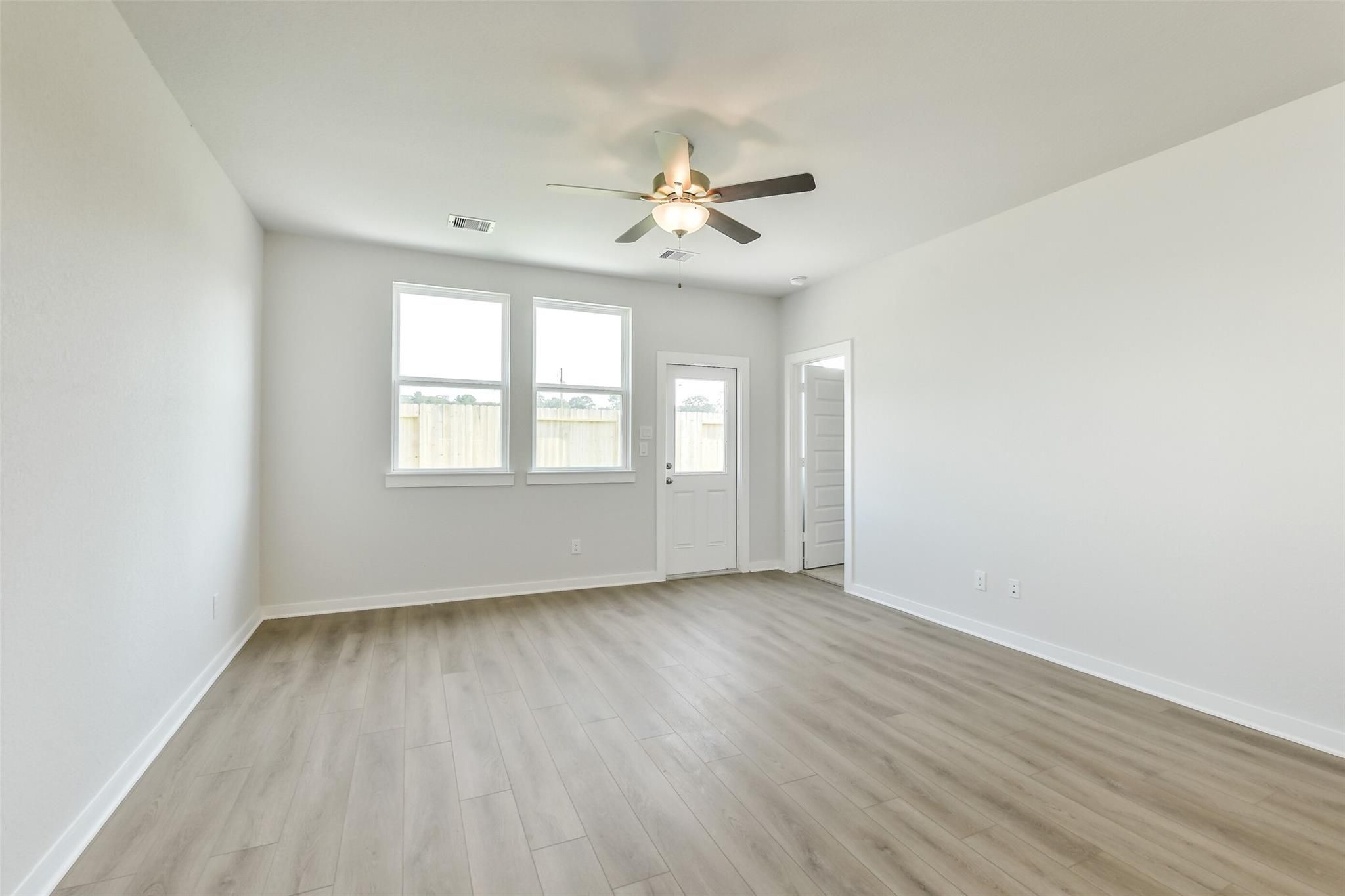 Bright living room with light wood floors, ceiling fans, and large windows in 4-bedroom Davidson Homes Colorado F, Cleveland TX