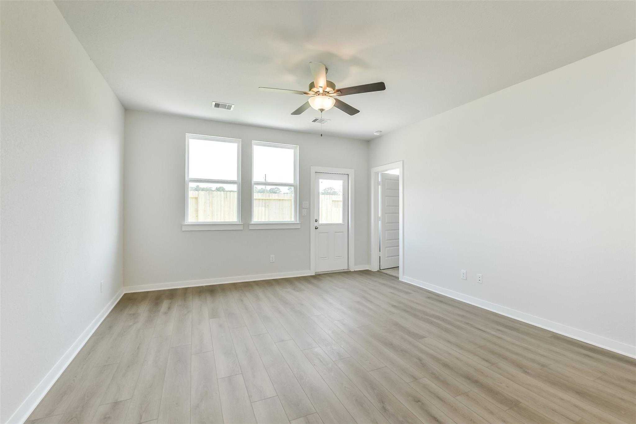 Bright open living room with ceiling fans, large windows, and hardwood floors in Davidson Homes The Colorado F, Cleveland, Texas