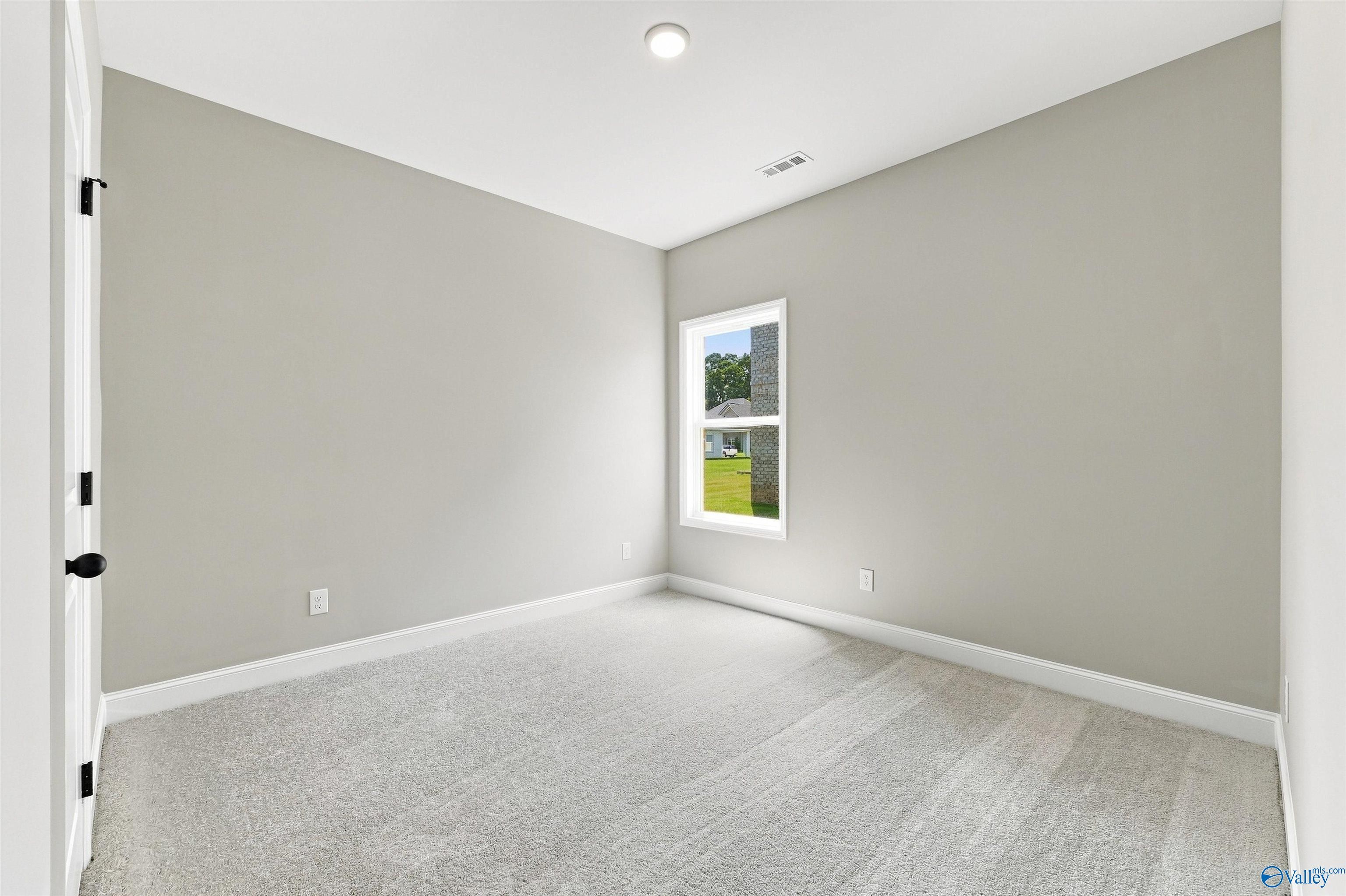Bright empty bedroom with neutral walls, carpet, and window overlooking yard in Davidson Homes Franklin C plan, Toney, AL
