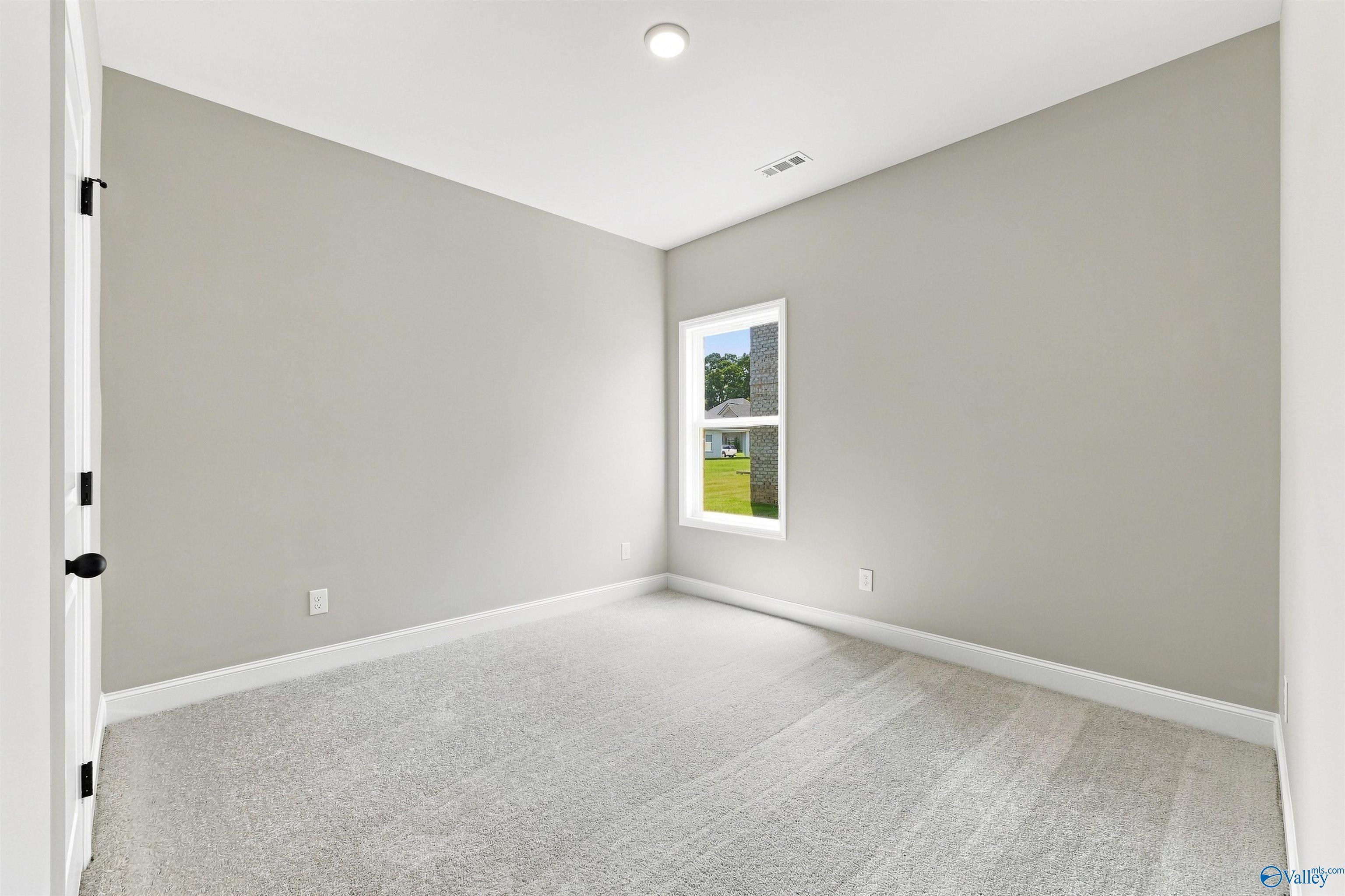 Bright empty bedroom with neutral walls, carpet, and window overlooking yard in Davidson Homes Franklin C plan, Toney, AL