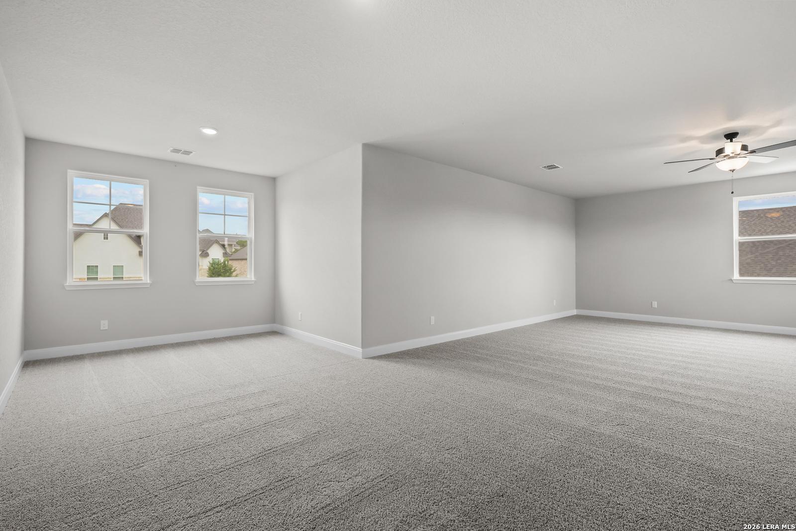 Spacious empty bedroom with gray walls, carpet, ceiling fan, and neighborhood views in Davidson Homes The Belmont H, Castroville, Texas