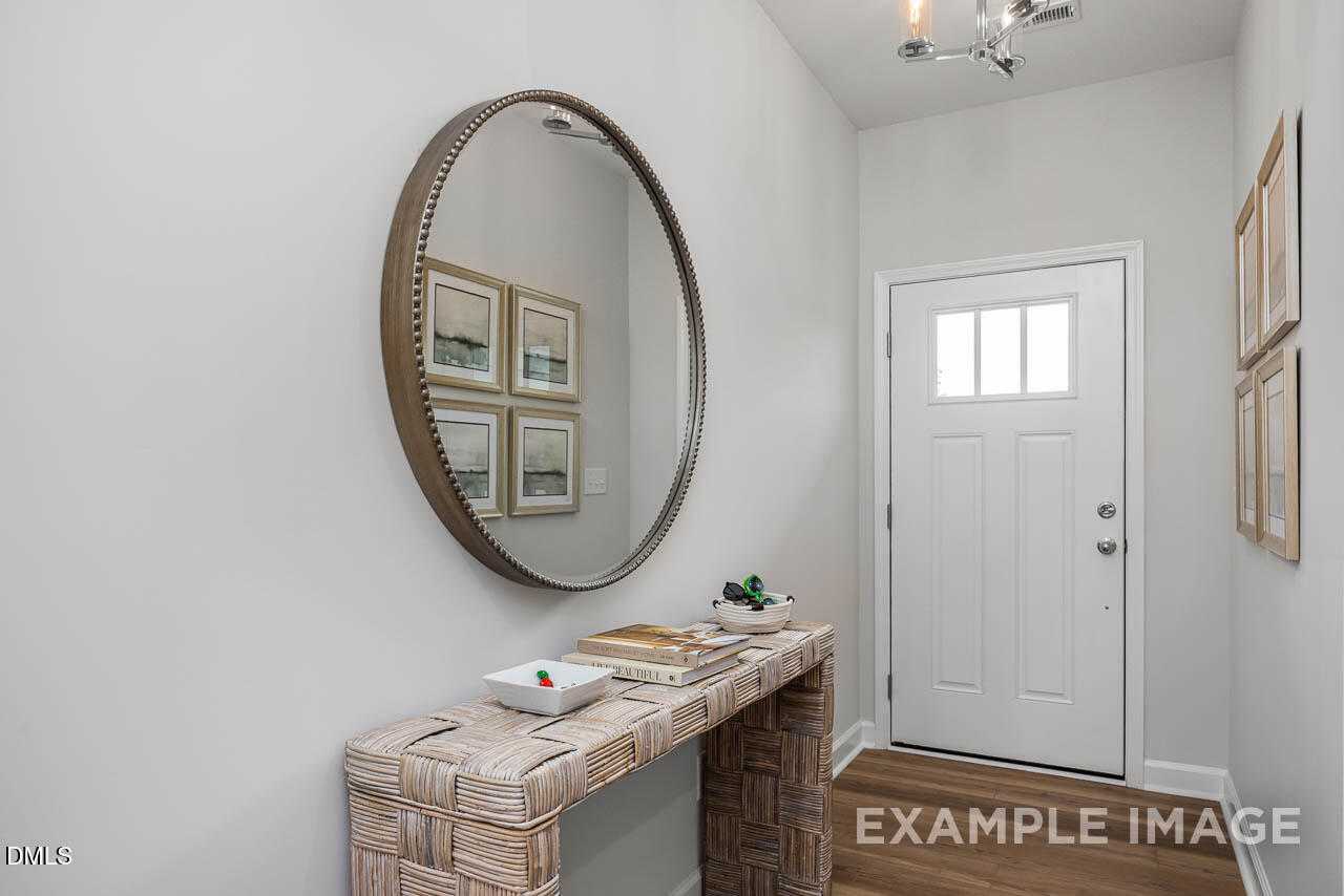 Elegant entryway featuring large round mirror, woven console table with decor, and white door in Davidson Homes The Graham, Fuquay-Varina, NC