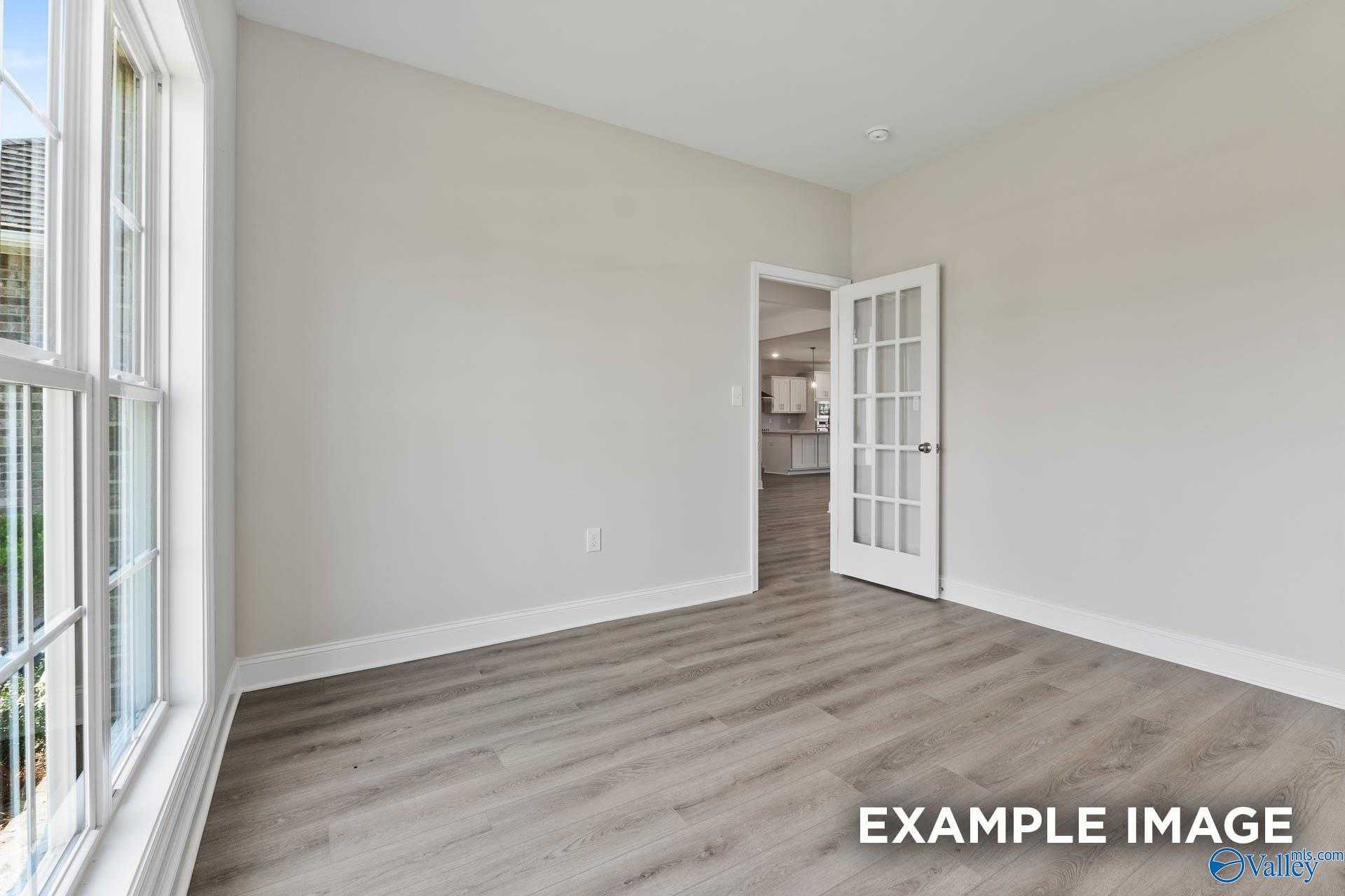 Bright empty living room with large windows, French doors to kitchen, and hardwood floors in Davidson Homes The Finleigh, Meridianville, AL