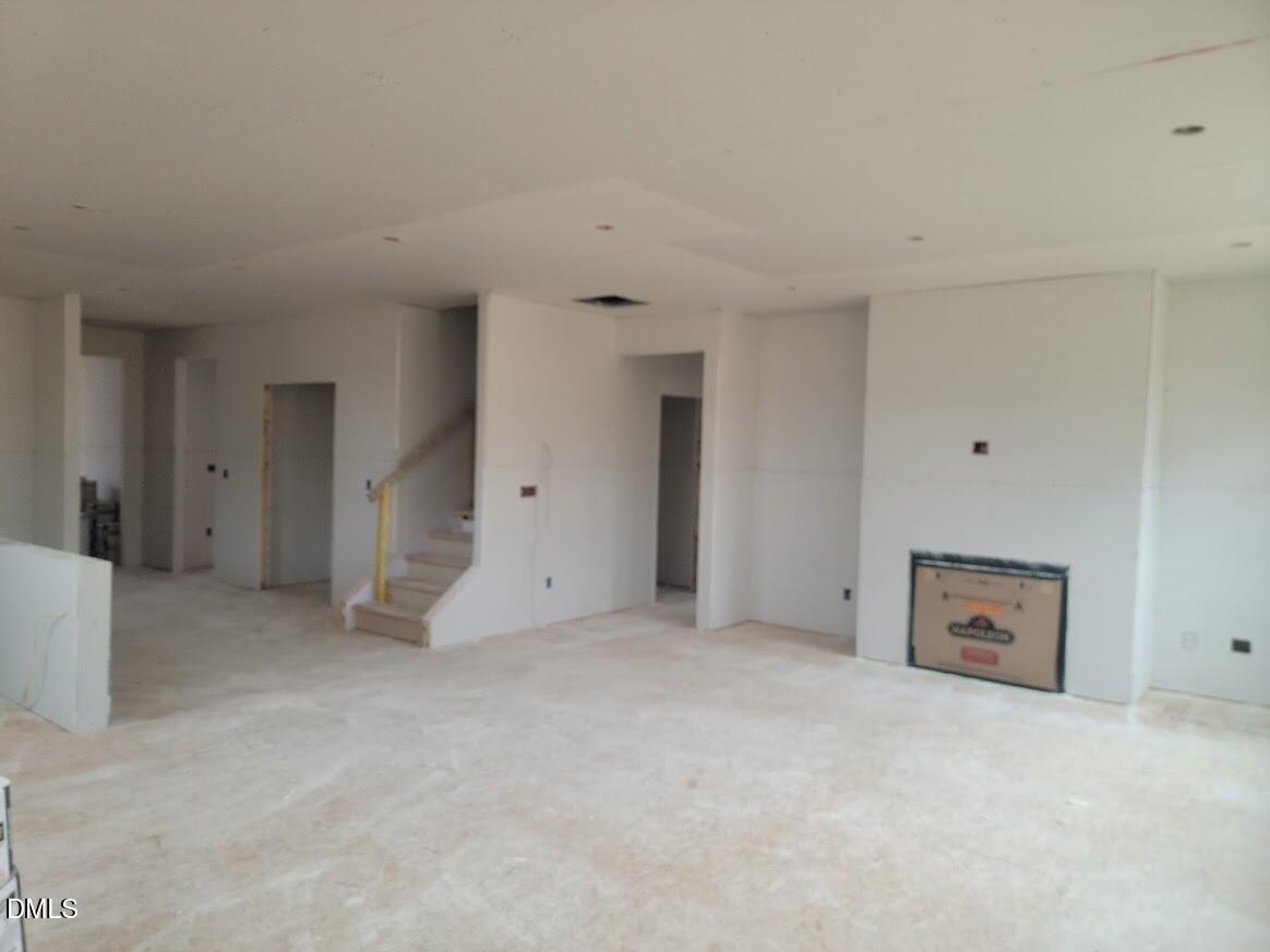 Spacious unfinished living room with open staircase, fireplace, and drywall in The Ashport G 5-bedroom home by Davidson Homes, Angier, NC