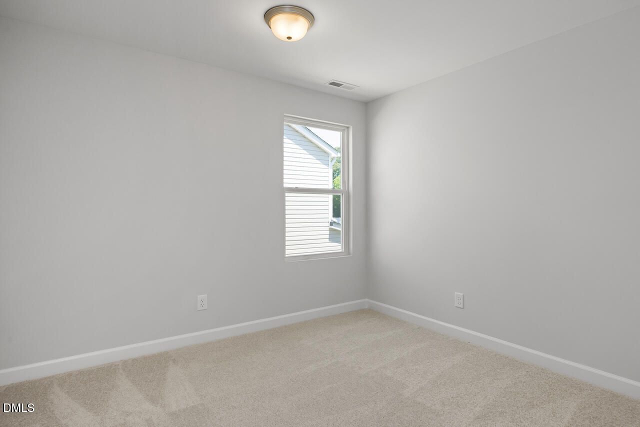 Bright, carpeted bedroom with neutral walls in The Adalynn A floor plan at Gregory Village in Lillington, North Carolina.