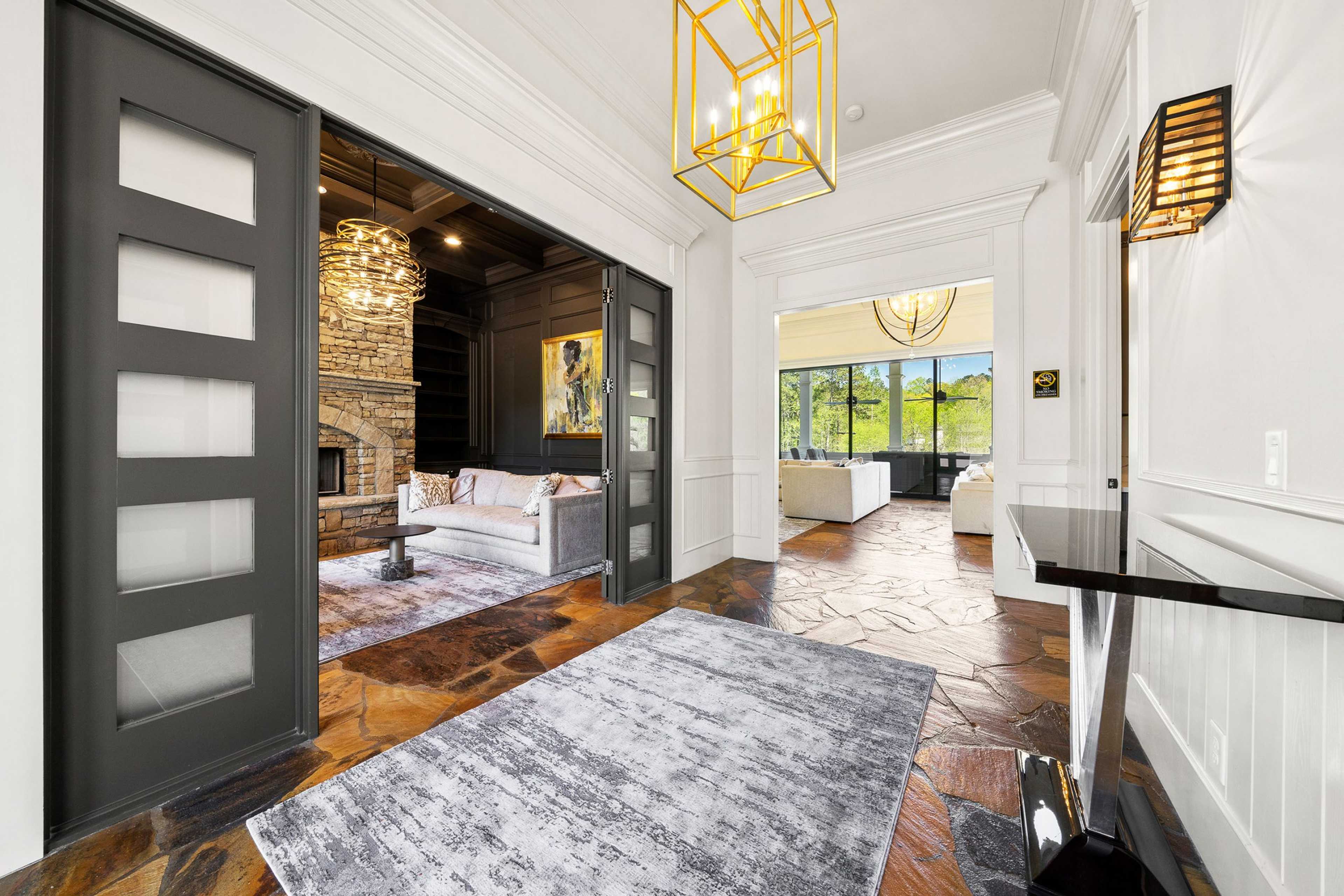 Spacious living room in Riverwood Dallas Georgia with stone fireplace, gold chandelier, and open wood-floored hallway
