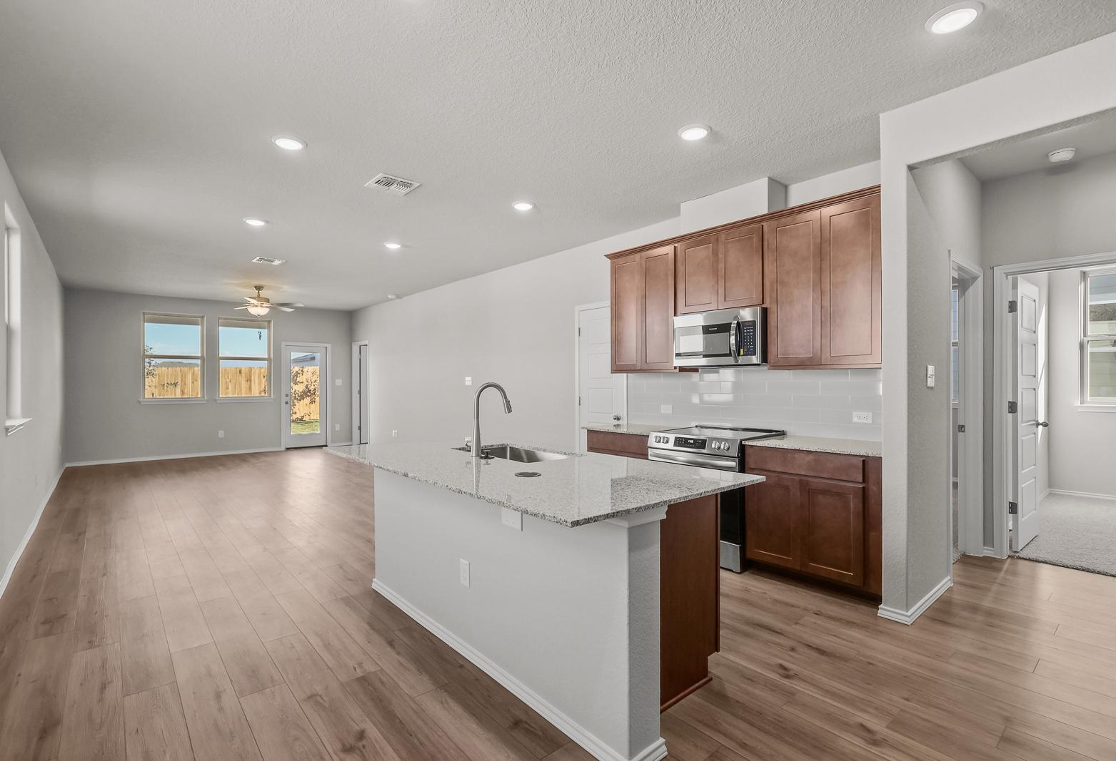 Open-concept kitchen and living area in The Arroyo floor plan featuring a center island and wood-style flooring.