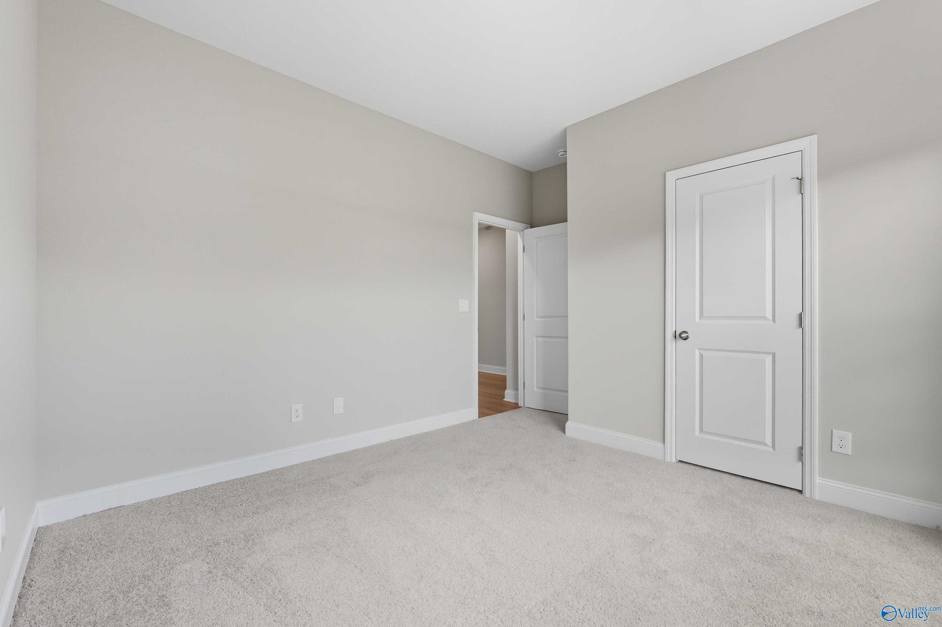 Empty bedroom featuring light gray walls, beige carpet, and white doors in Davidson Homes The Franklin, Meridianville, Alabama