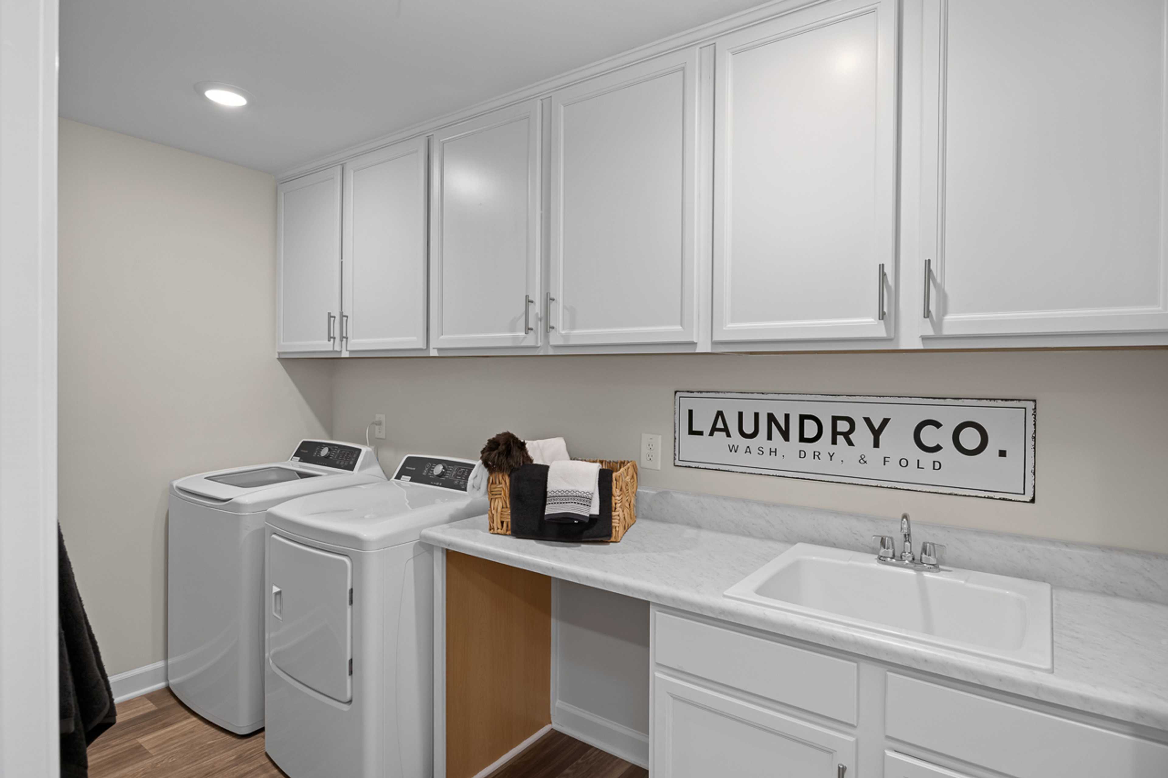 Modern laundry room in Wellers Knoll Lillington NC home by Davidson Homes with white shaker cabinets, washer dryer set, utility sink
