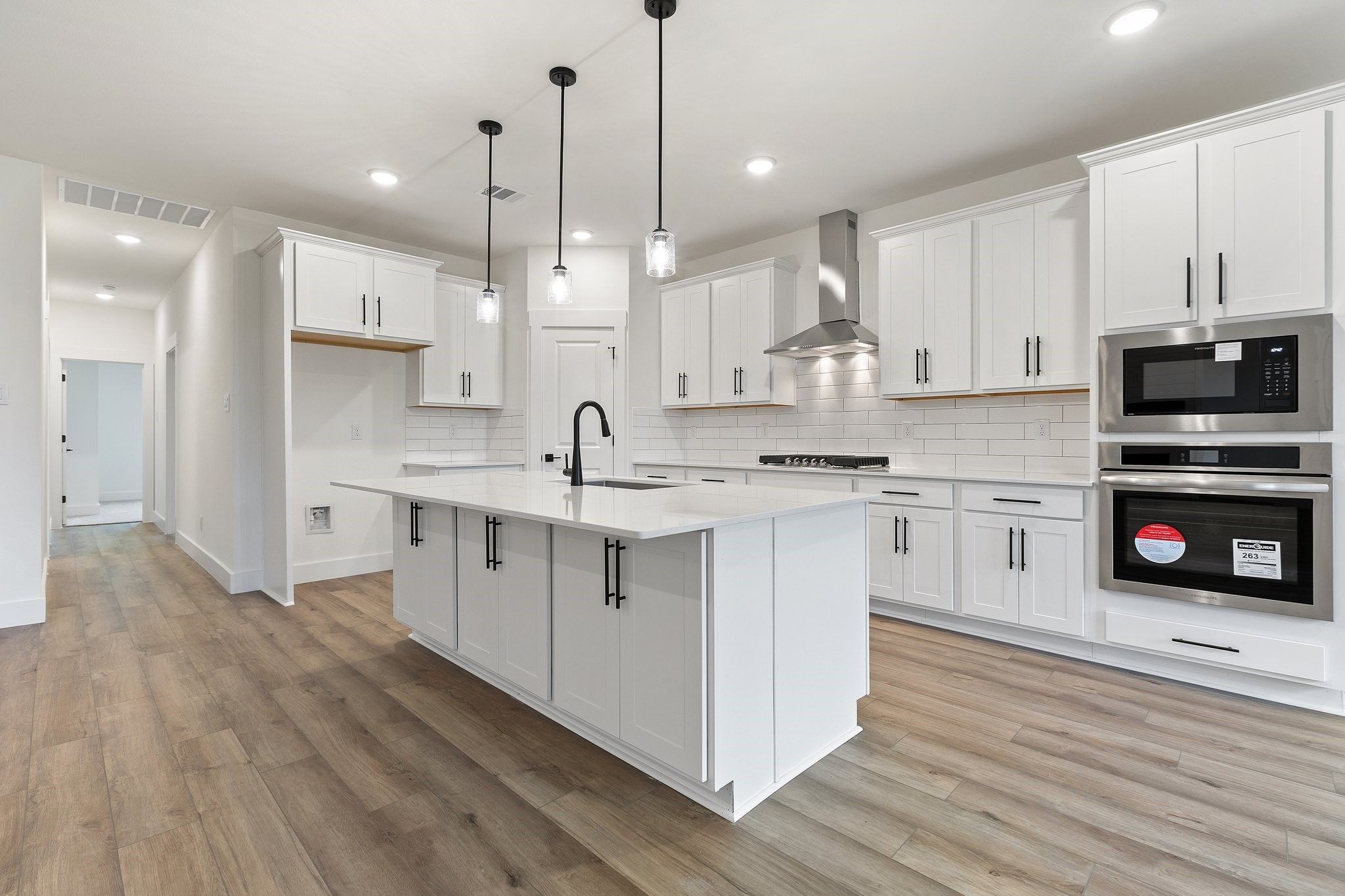 Modern white kitchen with island, pendant lights, and stainless appliances in The Rockford C plan, Waverly Estates, TX.