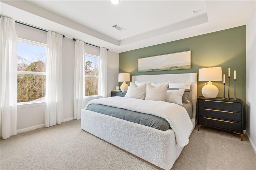 Elegant master bedroom with white tufted bed, green accent wall, tray ceiling, and wooded views in Davidson Homes The Rabun B, Canton, Georgia