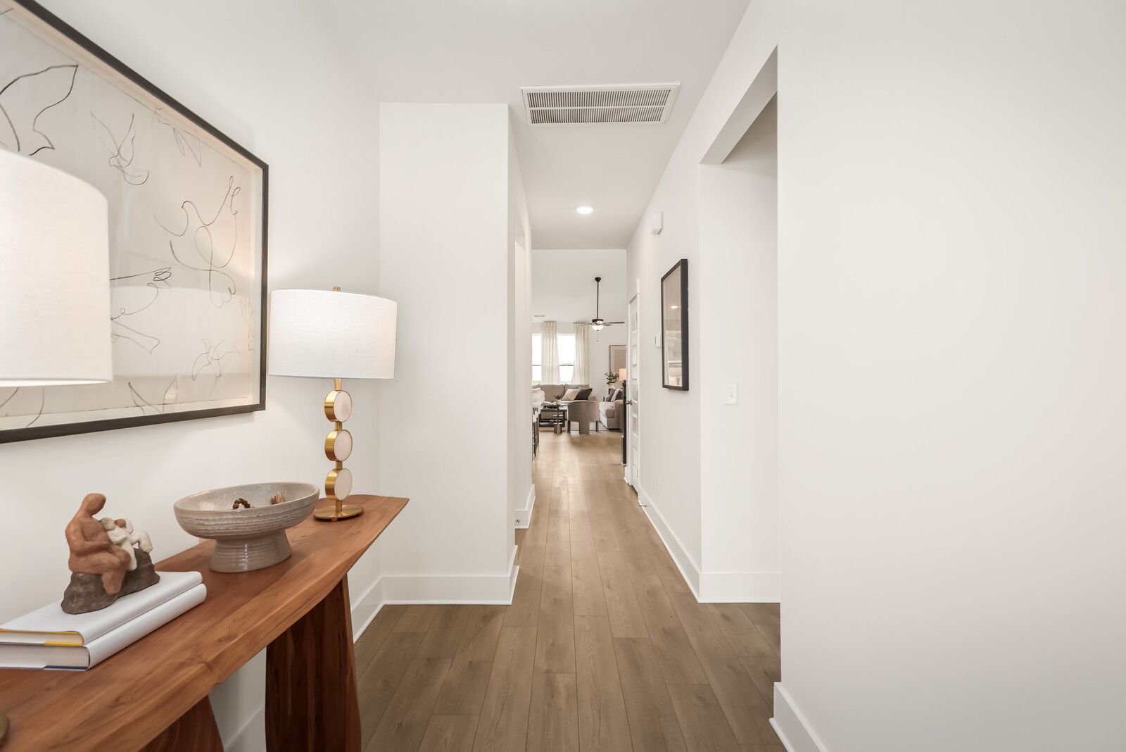 Spacious foyer in Benders Cove Mt. Juliet TN home by Davidson Homes with wooden console table, brass lamp, abstract art, and open hardwood hallway