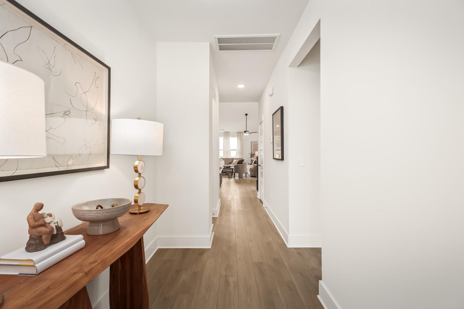 Spacious foyer in Benders Cove Mt. Juliet TN home by Davidson Homes with wooden console table, brass lamp, abstract art, and open hardwood hallway
