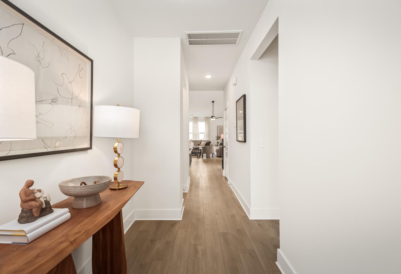 Bright entryway in The Ridgeport E showcasing wooden console table, abstract wall art, and open hallway to living area