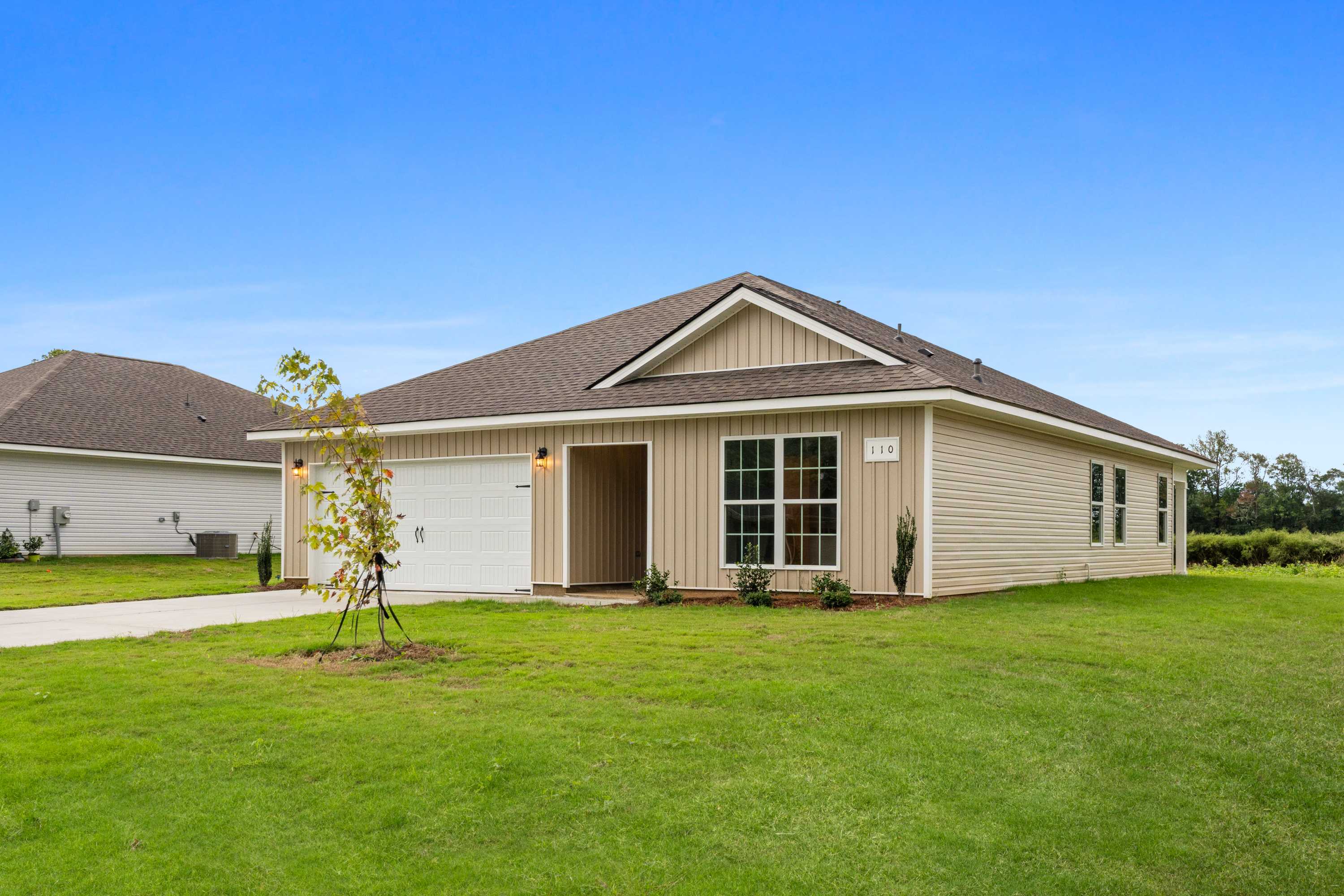 Tan sided single-story home exterior at Collins Lane in Meridianville Alabama with attached garage, gabled roof, and landscaped green yard