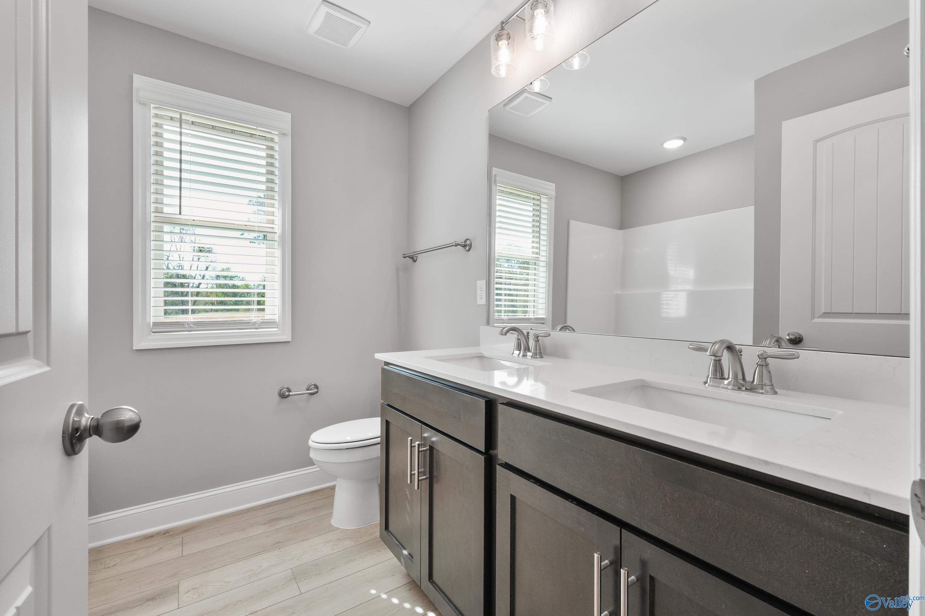 Modern double vanity bathroom with glass shower, gray walls, and wood floors in Davidson Homes Everett B, Athens Alabama