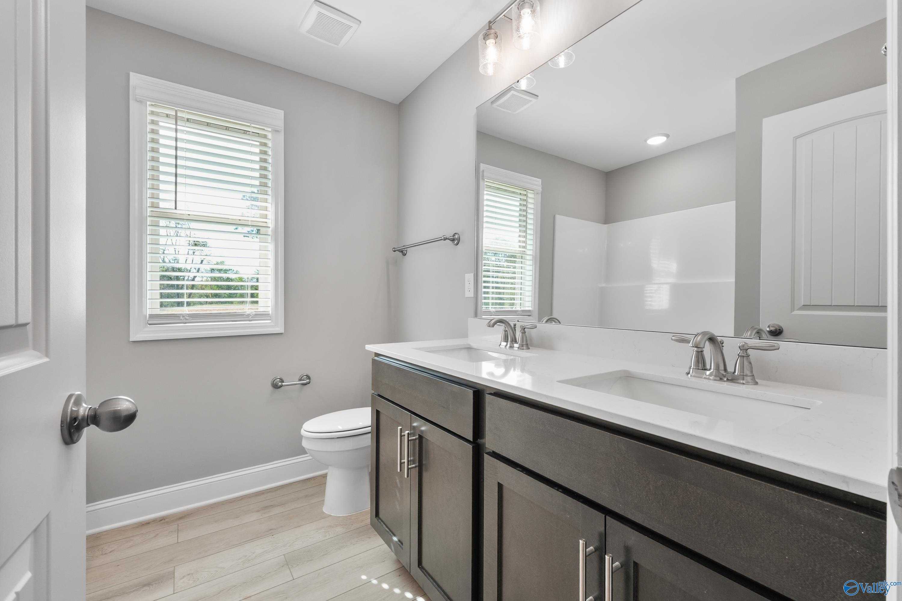 Elegant double vanity bathroom with shaker cabinets, glass shower, and natural light in Davidson Homes The Everett B, Athens AL