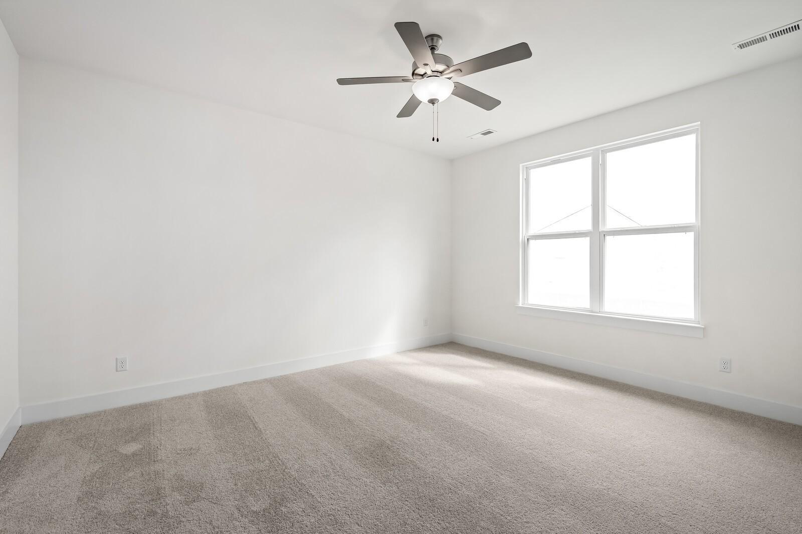 Bright secondary bedroom with ceiling fan, large window, and beige carpet in Davidson Homes The Ridgeport, Gallatin, TN