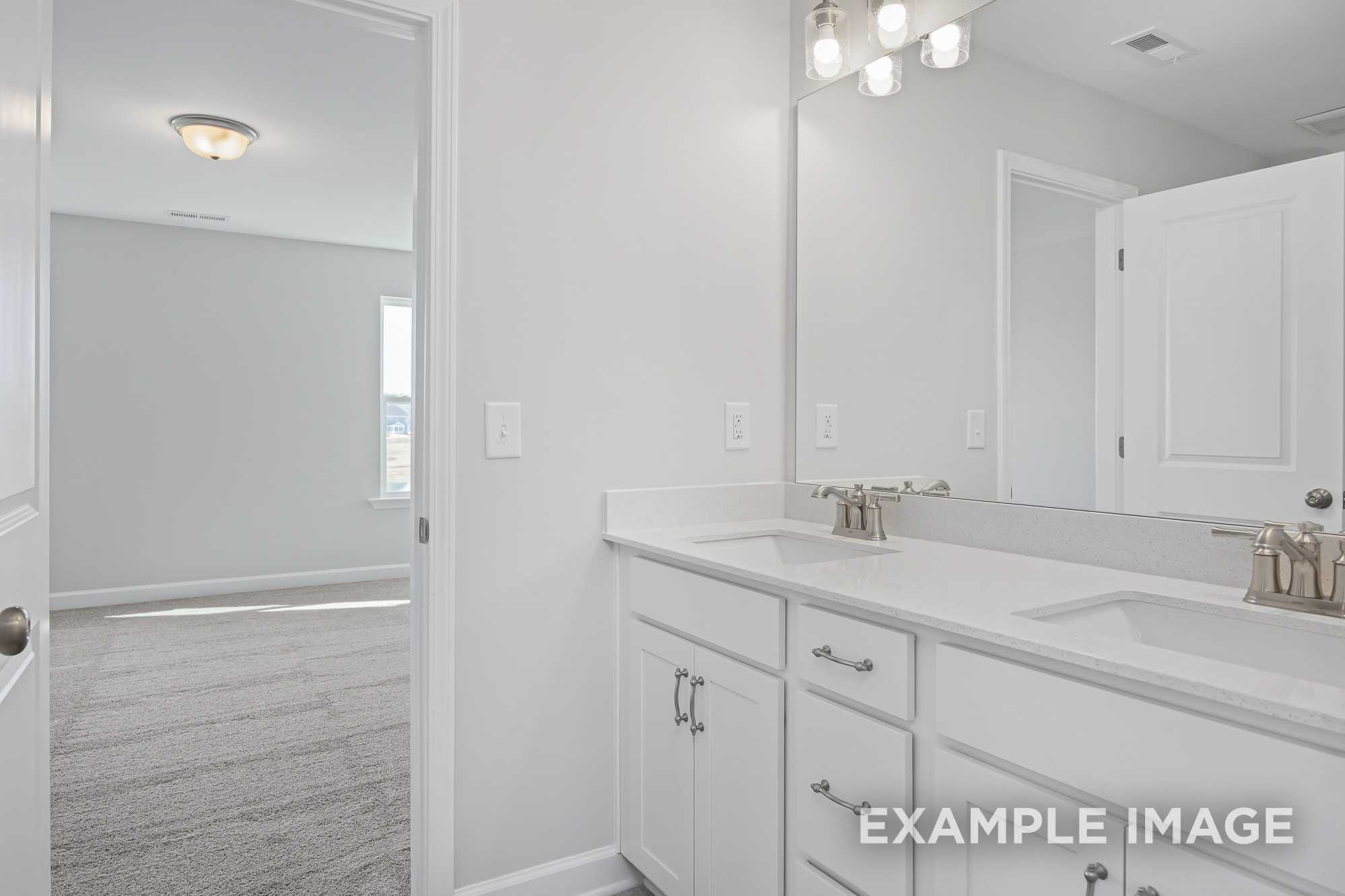 Spacious master bath in The Cypress D II with double white vanity, mirrors, and adjacent carpeted bedroom view