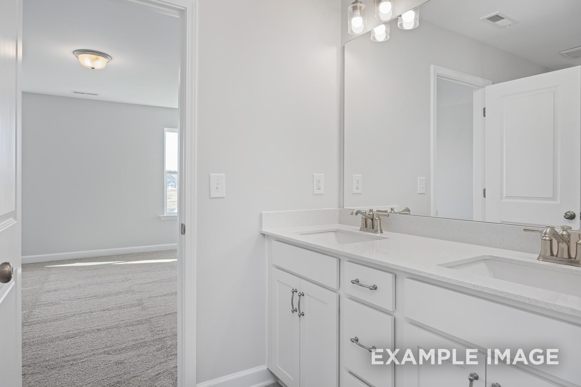 Spacious master bathroom in The Cypress C II featuring double white vanity, large mirror, and open bedroom door