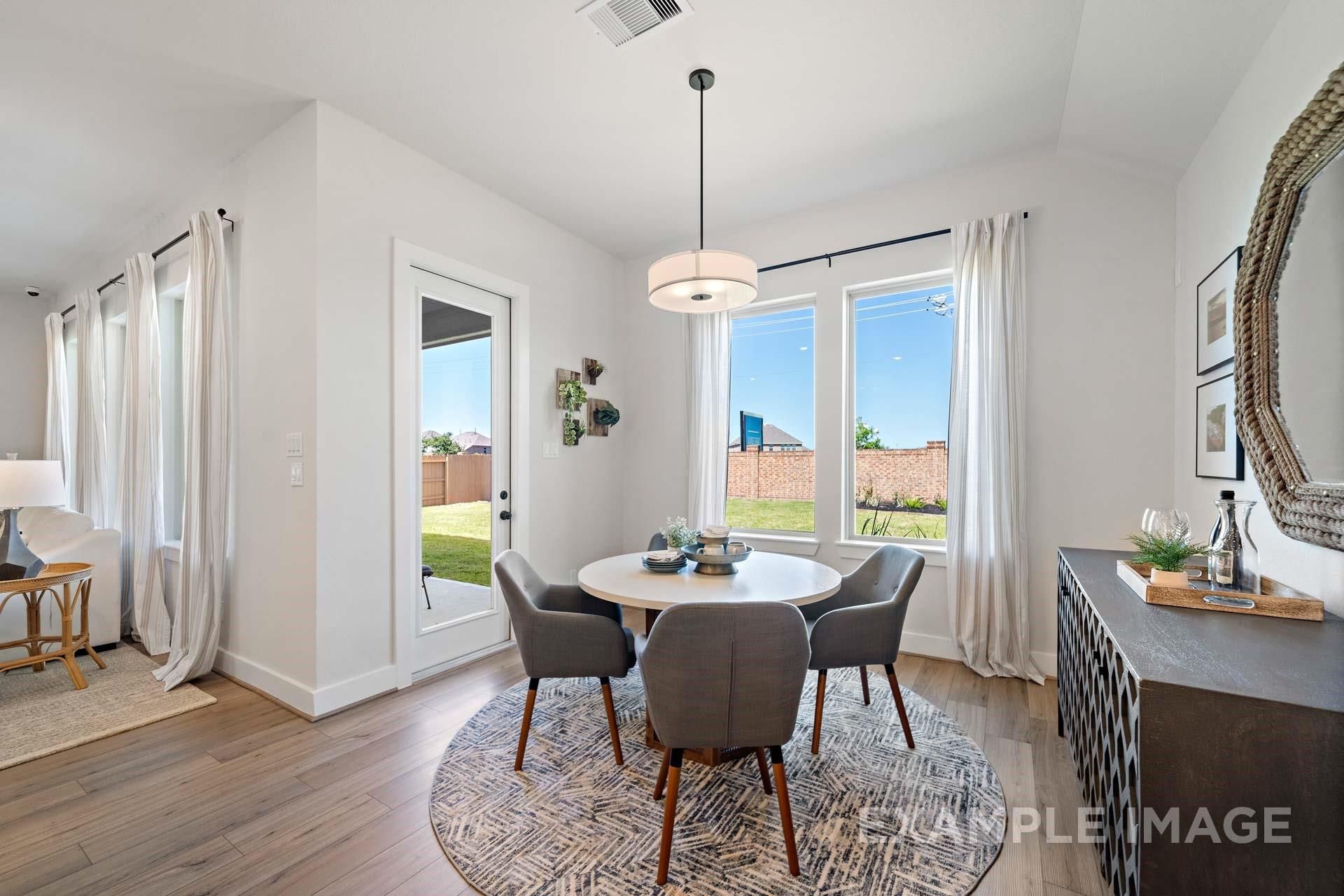 Modern dining room with round table, gray chairs, and chandelier overlooking lush backyard in The Edward A, Davidson Homes, Lago Mar, Texas City