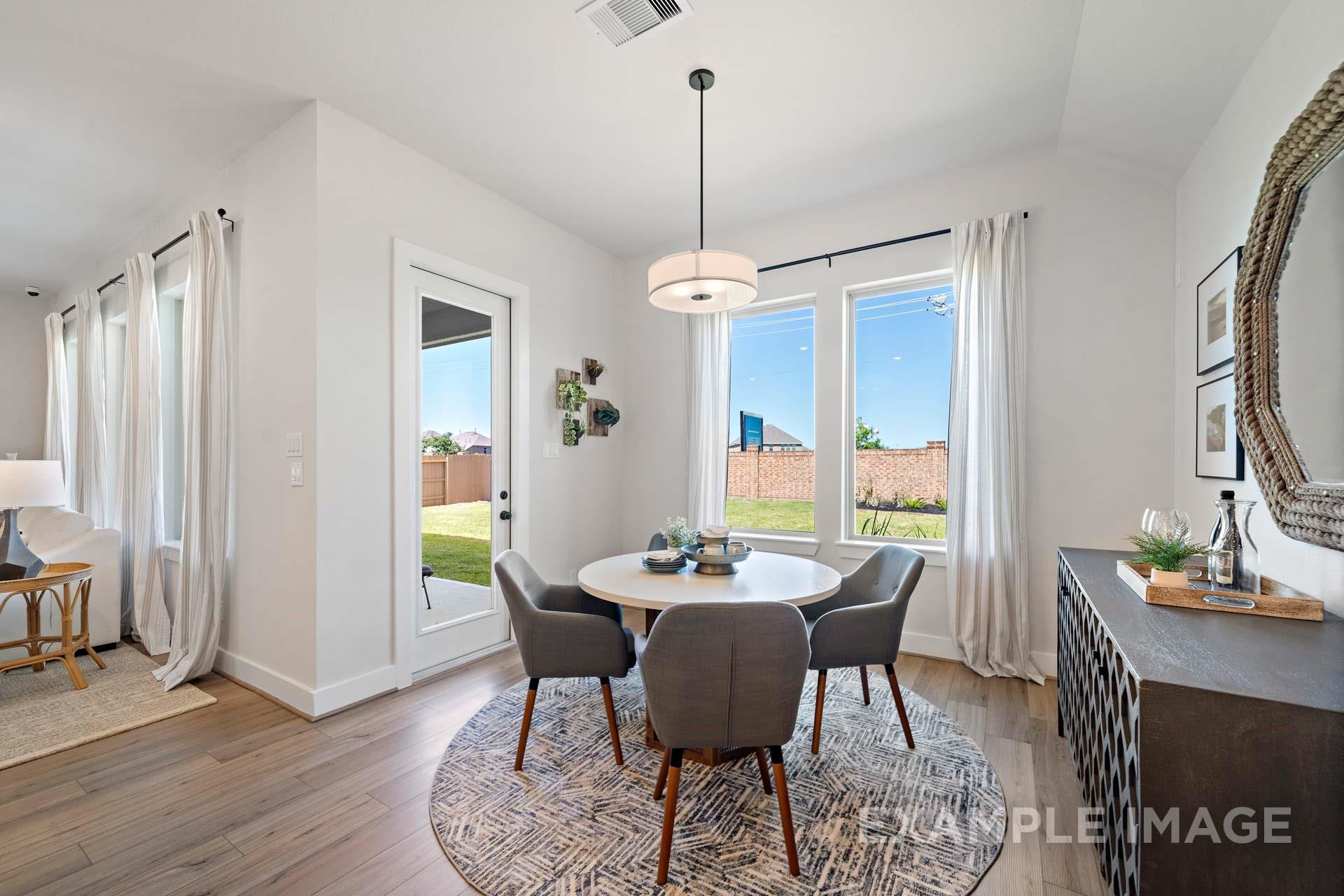 Modern dining room with round table, gray chairs, and chandelier overlooking lush backyard in The Edward A, Davidson Homes, Lago Mar, Texas City
