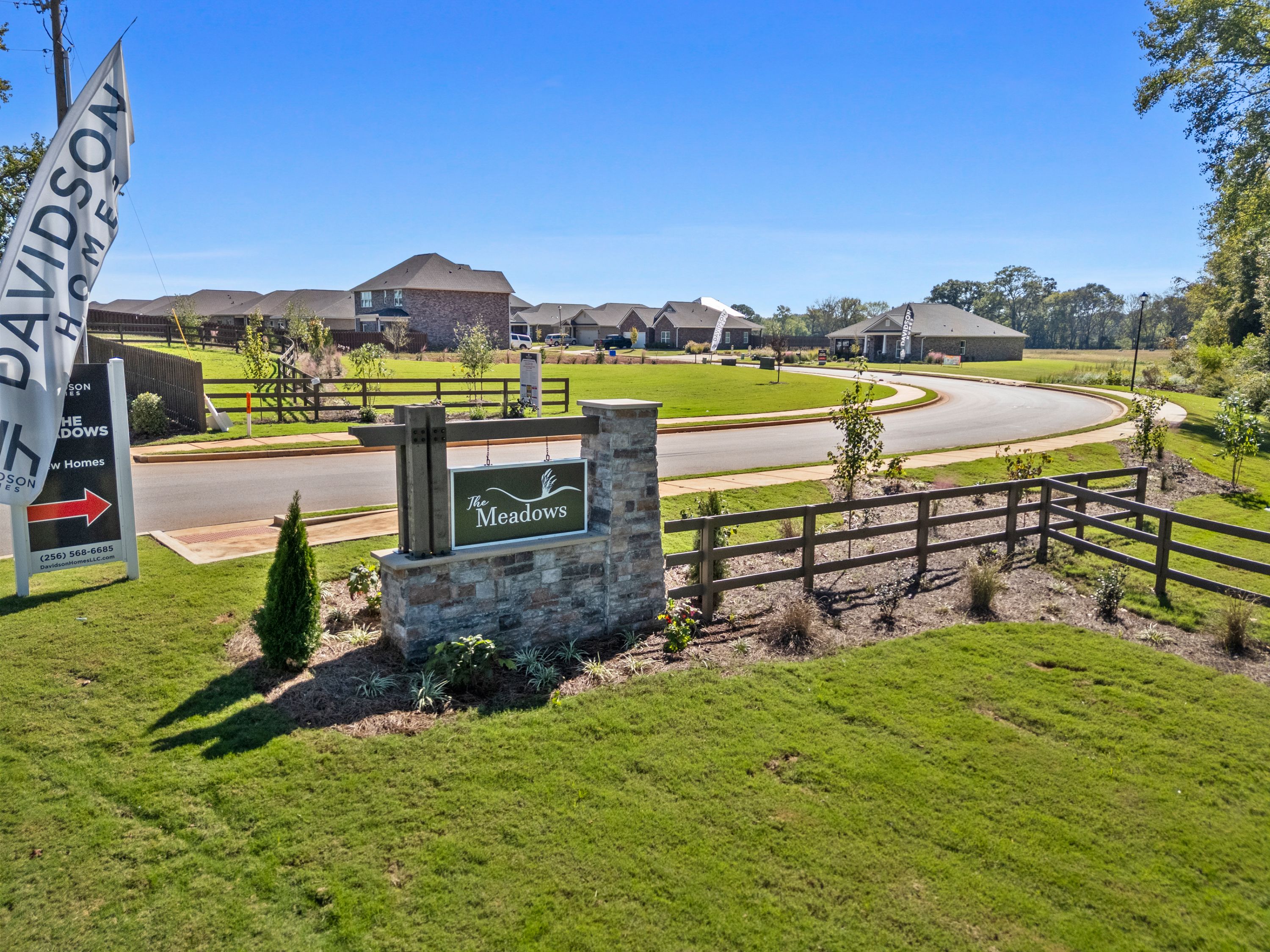 The Meadows entrance sign in Athens Alabama by Davidson Homes with lush greenery, curved road, and new brick homes