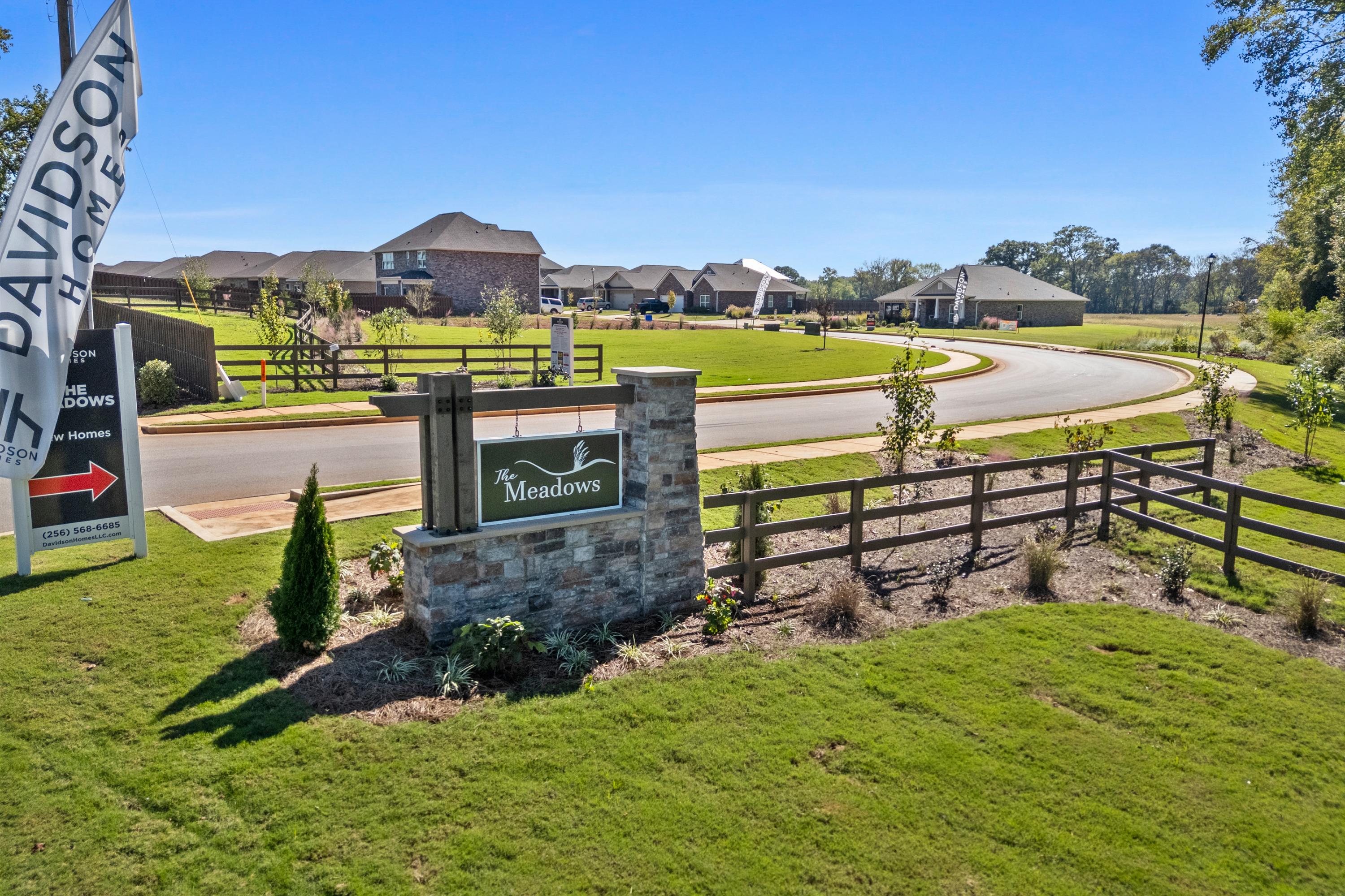 The Meadows entrance sign in Athens Alabama by Davidson Homes with lush greenery, curved road, and new brick homes