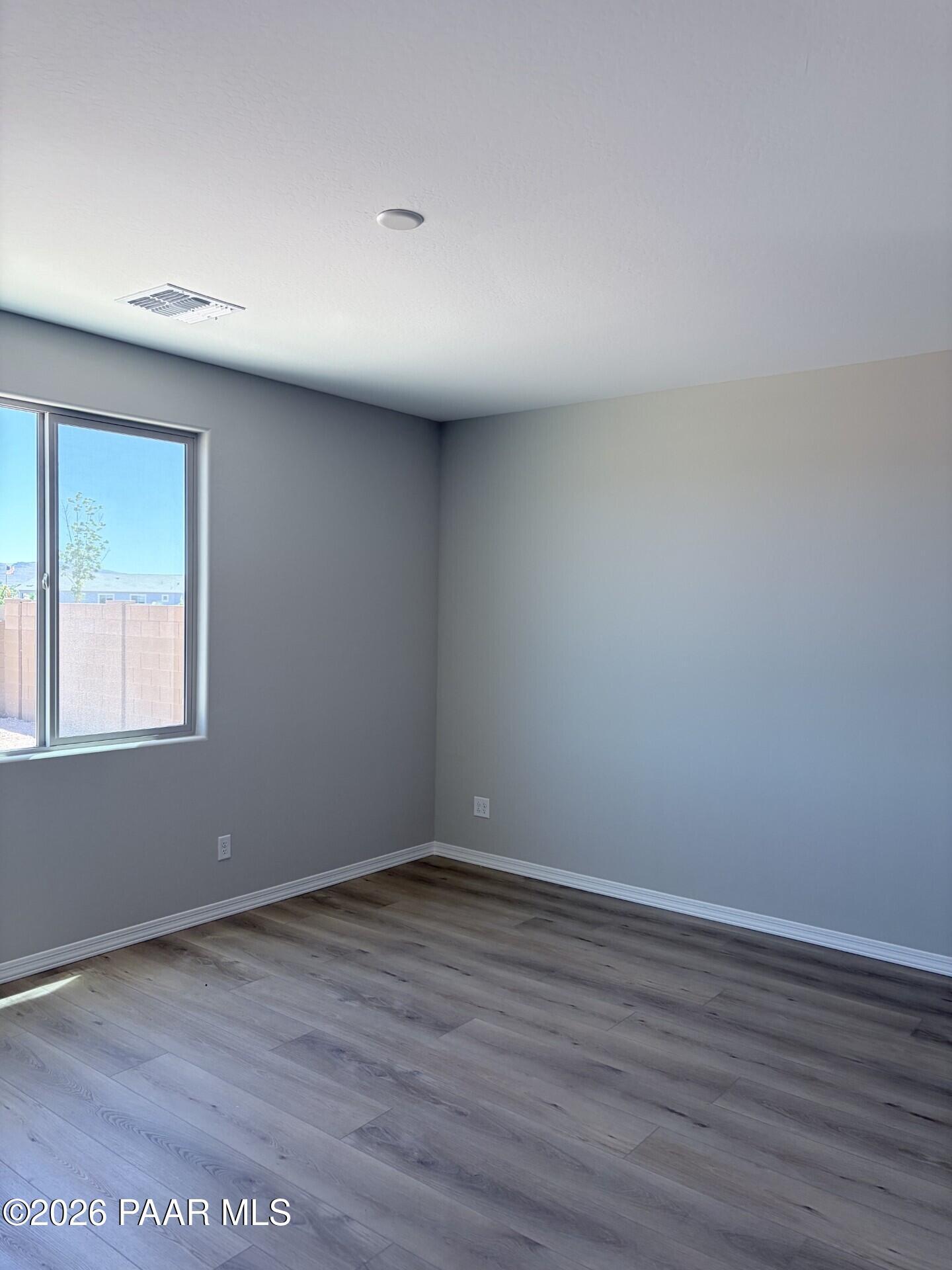 Spacious bedroom with grey walls and wood-look flooring in The Frontier A home at North Ridge, Pronghorn Ranch.