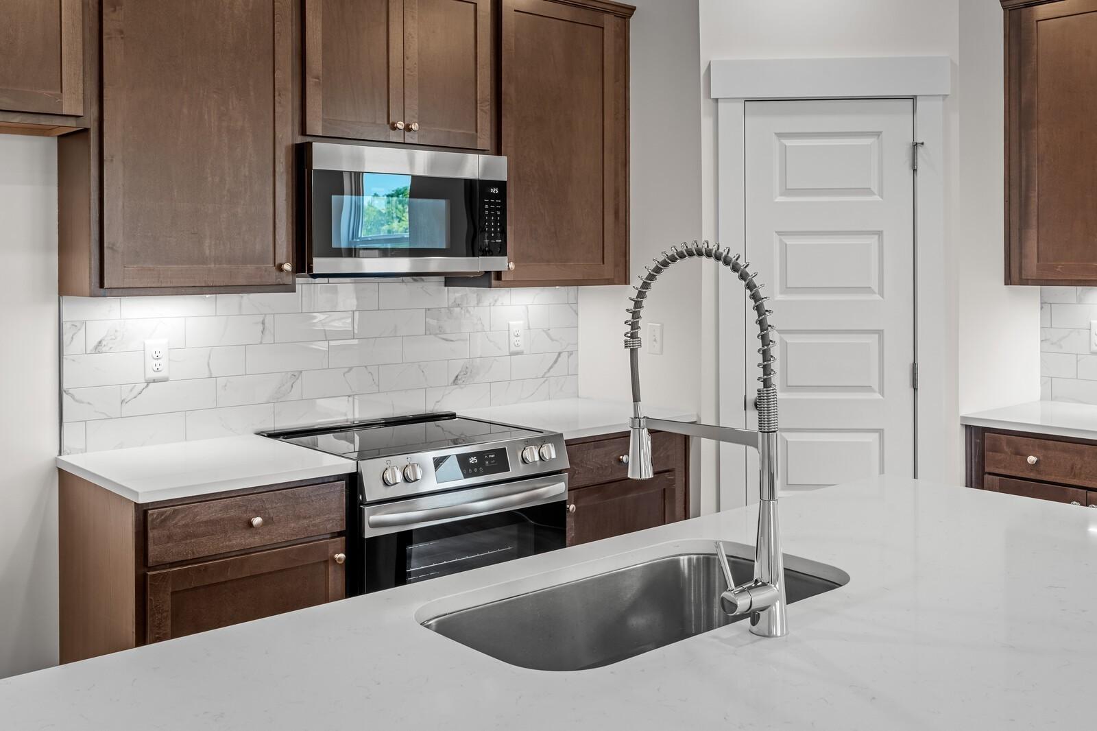 Modern kitchen with dark wood cabinets, white countertops, stainless appliances, and island sink in Davidson Homes Cottonwood E plan